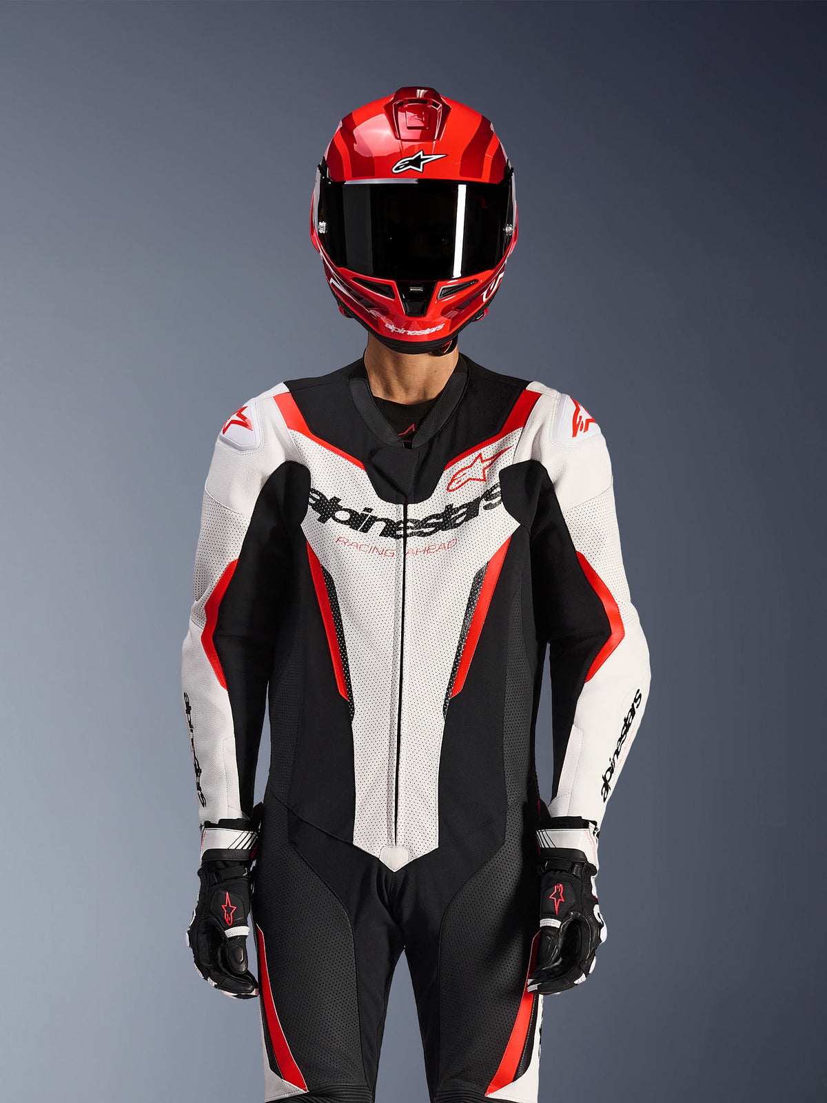 Alpinestars GP Force V2 Leather Suit - 1Piece, White Black Red Fluo, worn with red full-face helmet and black racing gloves, featuring perforated leather panels and bold Alpinestars branding on the chest, professional performance gear for motorcycle racing