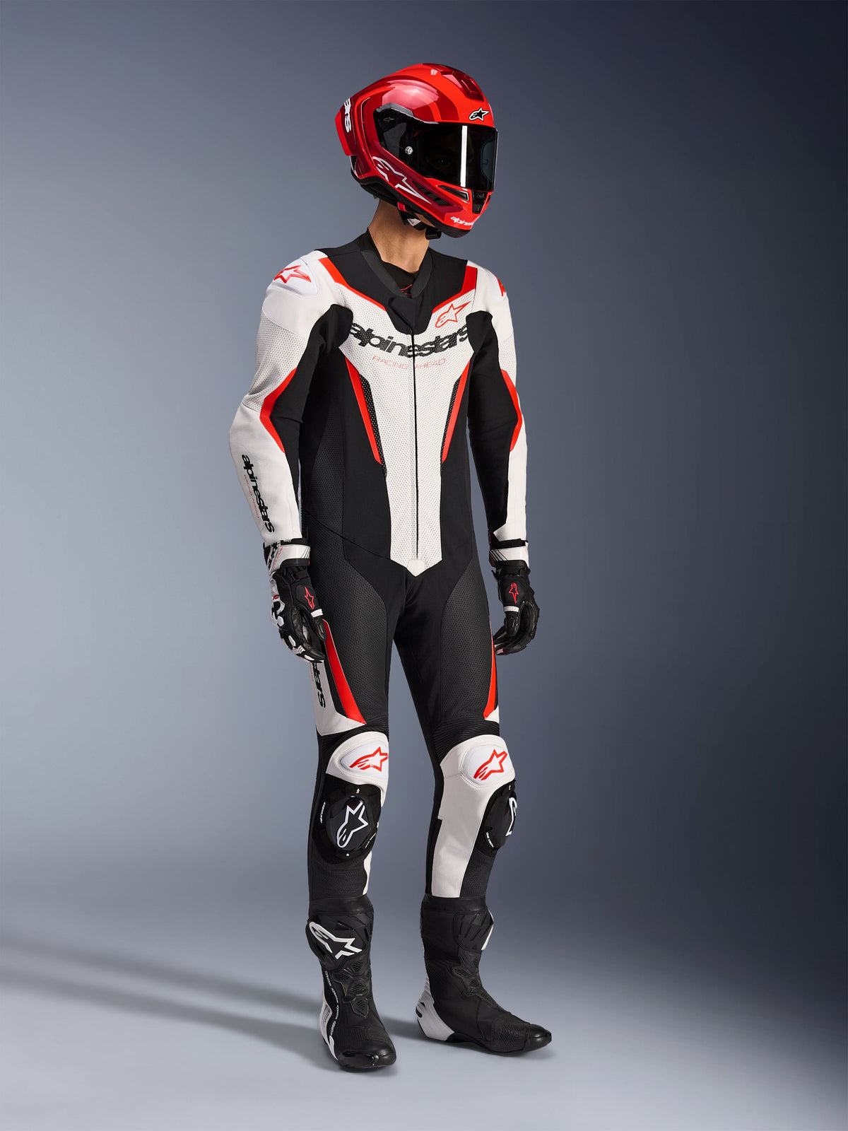 Alpinestars GP Force V2 Leather Suit 1-Piece in White Black and Red Fluo, full-body studio shot of a rider wearing complete racing gear including a red helmet, black gloves, and black boots, featuring aerodynamic bovine leather construction with bold branding and integrated knee sliders.