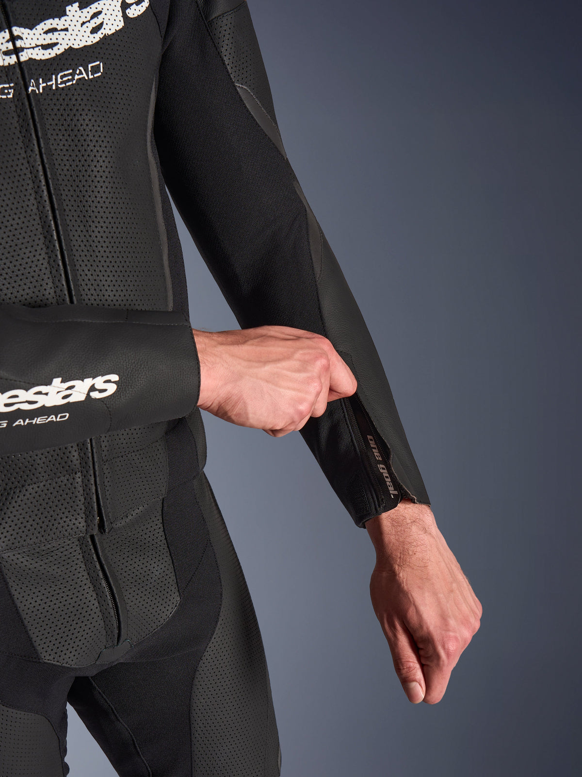 Alpinestars GP Force V2 2-Piece Leather Suit in Black, detail shot of the zippered forearm opening being adjusted, featuring perforated leather panels and stretch fabric construction.