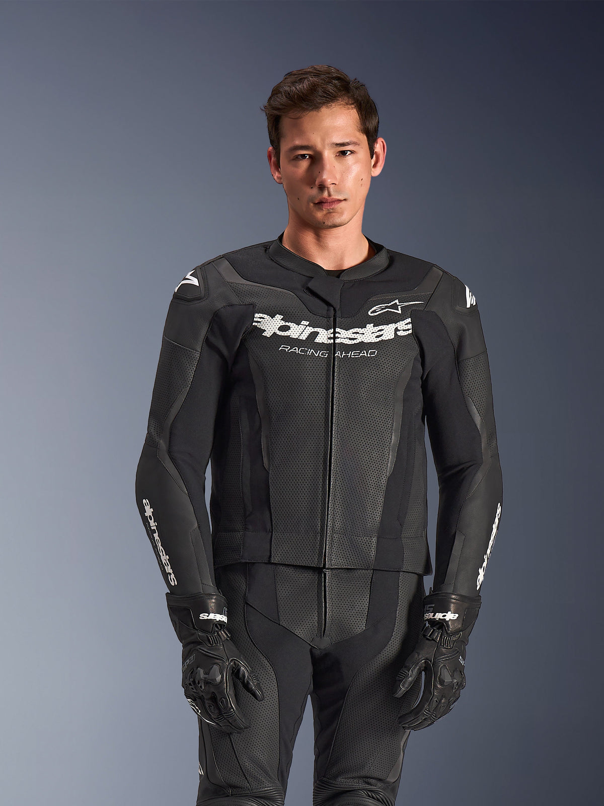 Alpinestars GP Force V2 Leather Suit 2-Piece, Black, worn by model, featuring perforated leather panels and white 'Alpinestars Racing Ahead' chest branding, paired with black gloves, professional sport riding gear