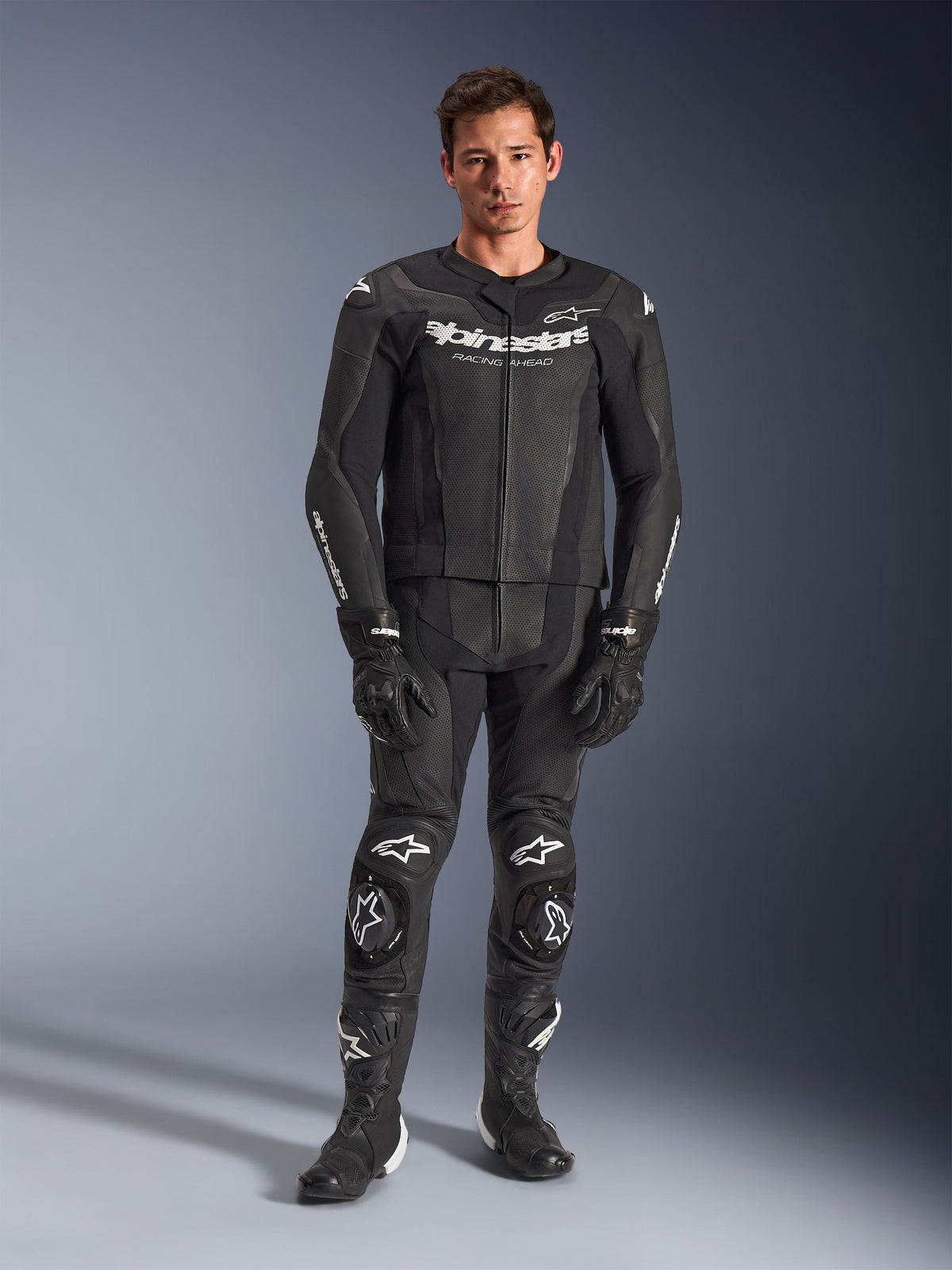 Alpinestars GP Force V2 Leather Suit 2-Piece, Black with white logos, full-body motorcycle racing suit, featuring premium leather construction with reinforced knee sliders and perforated panels, worn with black gloves and boots, studio full-length view
