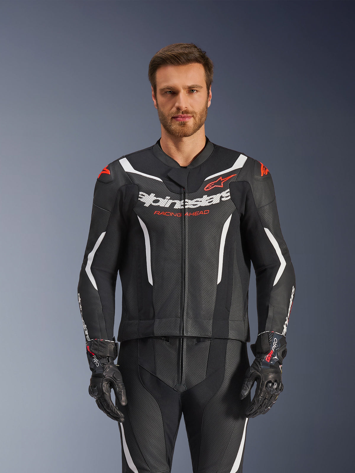 Alpinestars GP Force V2 Leather Suit- 2Piece, Black White and Red Fluo, front view of male model wearing the perforated leather suit with matching black gloves, featuring white angular accents and Alpinestars branding on the chest