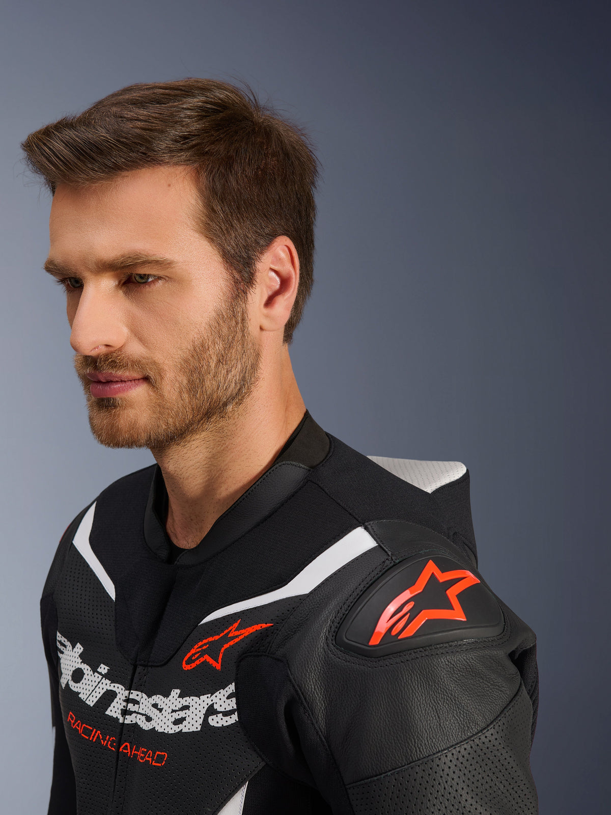 Alpinestars GP Force V2 Leather Suit 2-Piece, Close-up of jacket worn by male model, Black White and Red Fluo, featuring perforated leather, red star logo on the shoulder, aerodynamic speed hump, and Alpinestars branding on the chest, professional motorcycle racing gear
