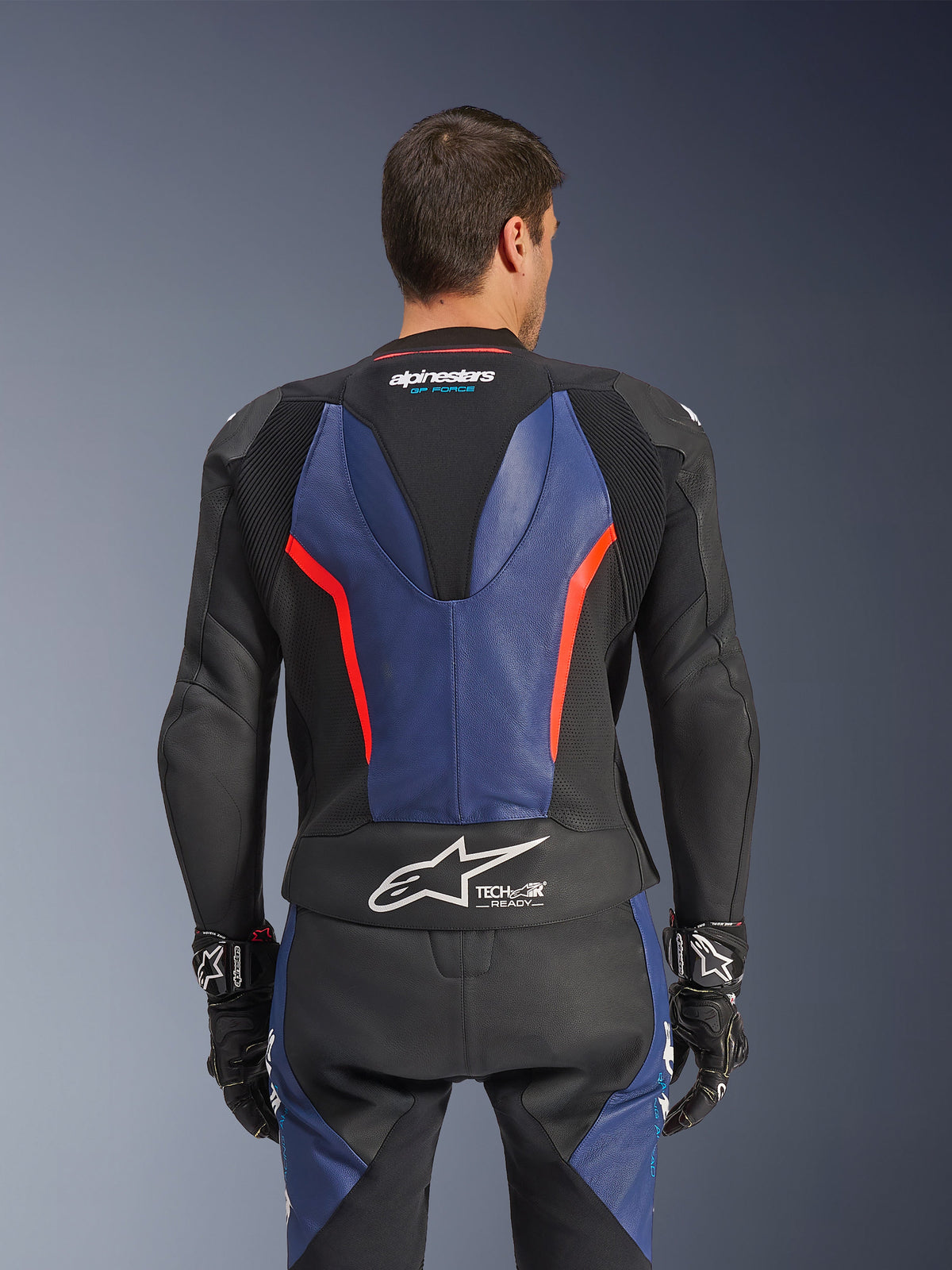 Alpinestars GP Force V2 Leather Suit 2-Piece, Back view, Black with Blue and Red Fluo accents, featuring perforated leather construction, Tech-Air Ready branding on the waist, and ergonomic stretch panels for racing performance.