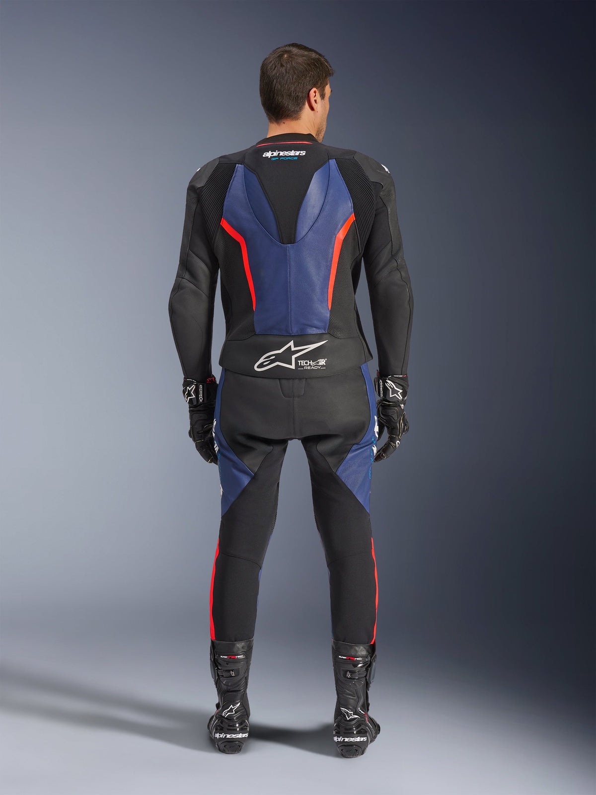 Alpinestars GP Force V2 Leather Suit 2-Piece, Rear View, Black Blue and Red Fluo, featuring blue leather panels on the back and legs with fluorescent red accents, Tech-Air Ready branding on the lower back, worn with black racing gloves and boots.