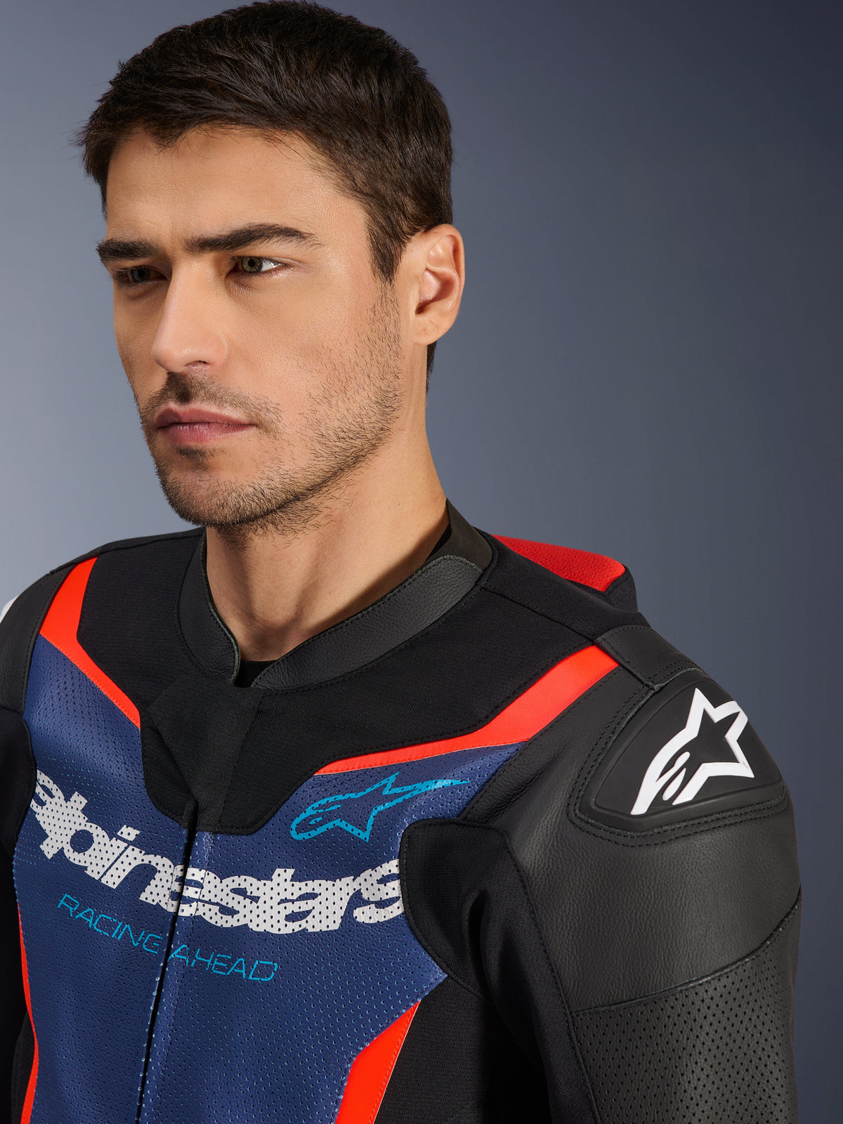 Alpinestars GP Force V2 Leather Suit- 2Piece, Black Blue and Red Fluo, close-up of a model wearing the suit jacket, featuring perforated bovine leather panels, Alpinestars logo on the shoulder, and 'Racing Ahead' branding on the chest, professional-grade racing gear