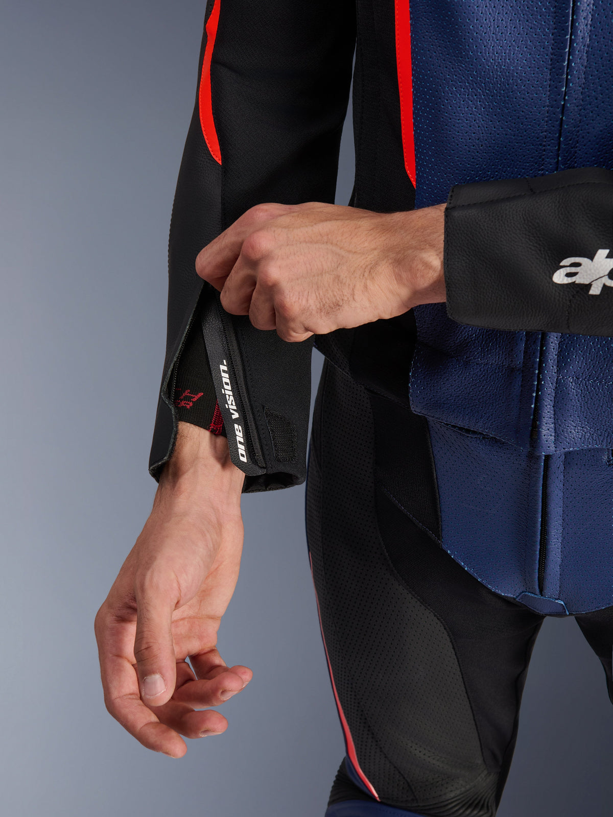 Alpinestars GP Force V2 Leather Suit 2-Piece, close-up detail of the sleeve cuff and torso, Black Blue and Red Fluo, featuring perforated leather, zippered wrist with "one vision" branding, and red fluorescent accents, professional sport riding gear