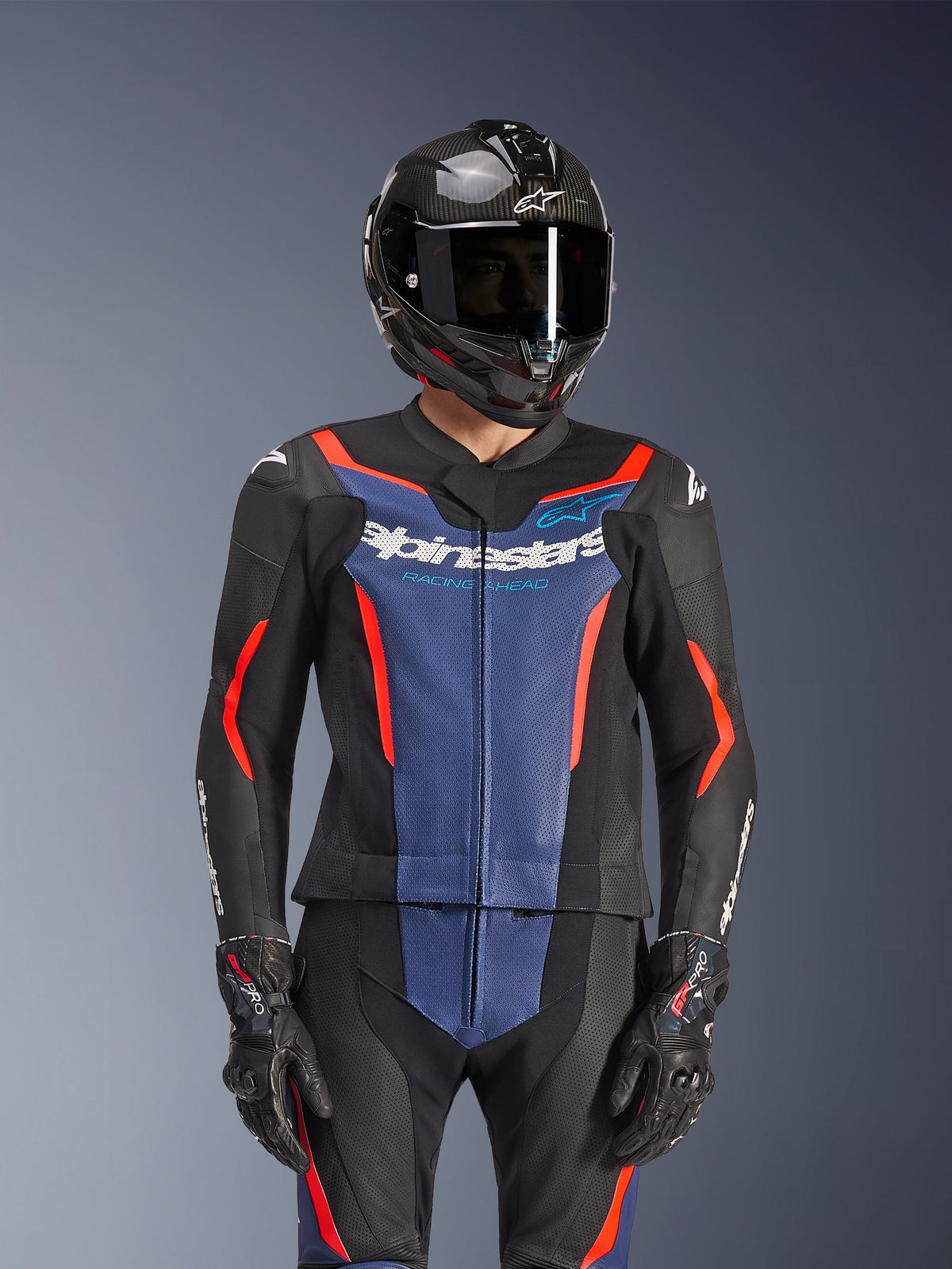 Alpinestars GP Force V2 Leather Suit 2-Piece, Black Blue and Red Fluo, worn with a carbon fiber helmet and racing gloves, featuring perforated leather panels and white Alpinestars logo on the chest, professional racing and sport riding gear