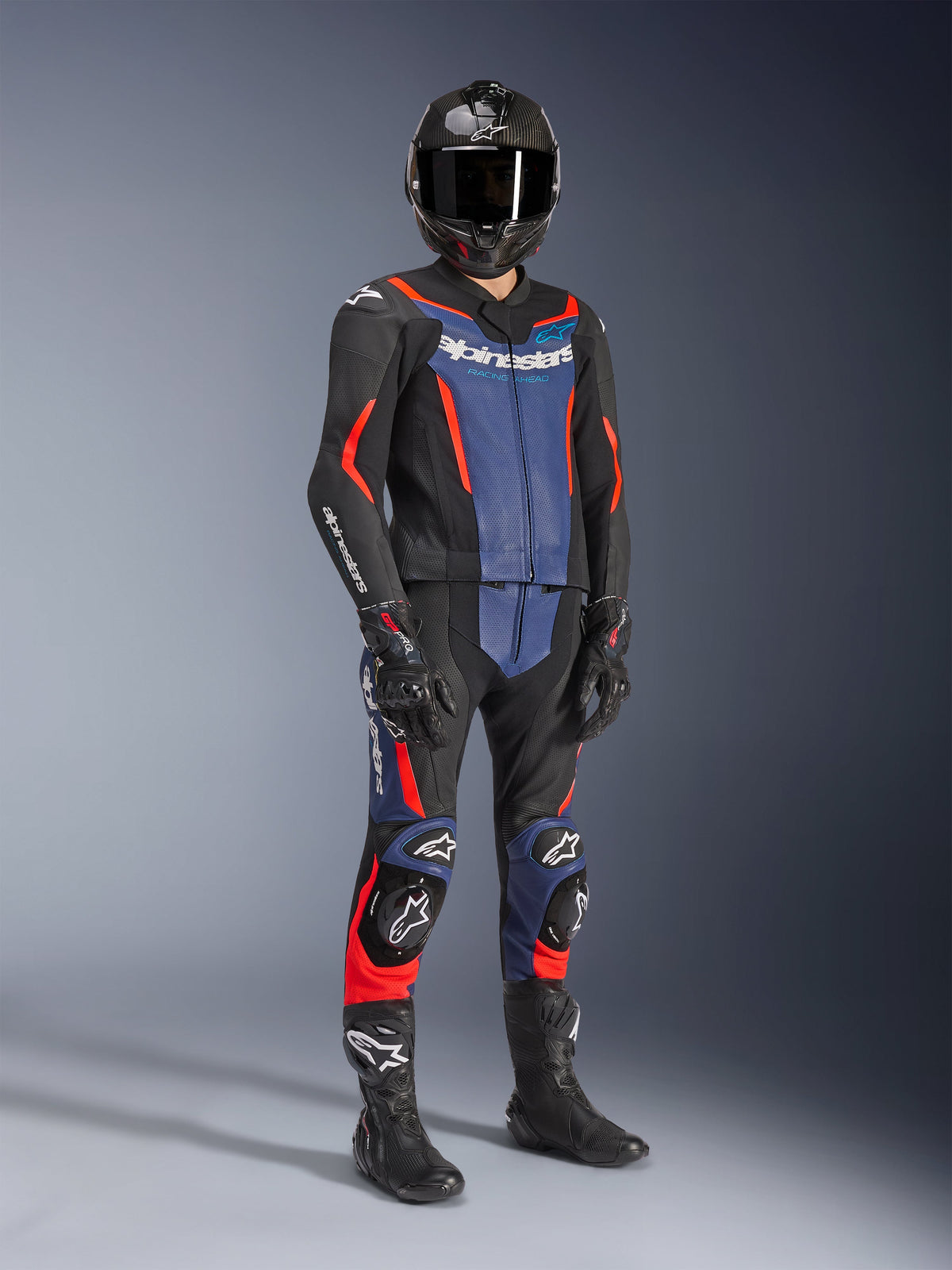 Alpinestars GP Force V2 Leather Suit - 2Piece in Black, Blue, and Red Fluo, worn with a carbon fiber helmet, black racing gloves, and boots, featuring perforated leather panels and white Alpinestars logo, professional sport riding gear.