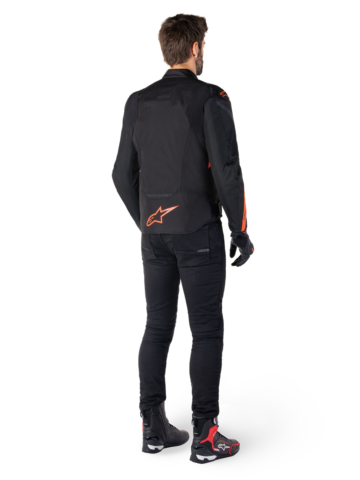 Alpinestars T-Jaws V4 Waterproof Jacket, czarno-czerwona fluo, widok z tyłu na motocykliście, z jaskrawym czerwonym logo na plecach, stylizacja z czarnymi spodniami i butami technicznymi, sportowa odzież motocyklowa