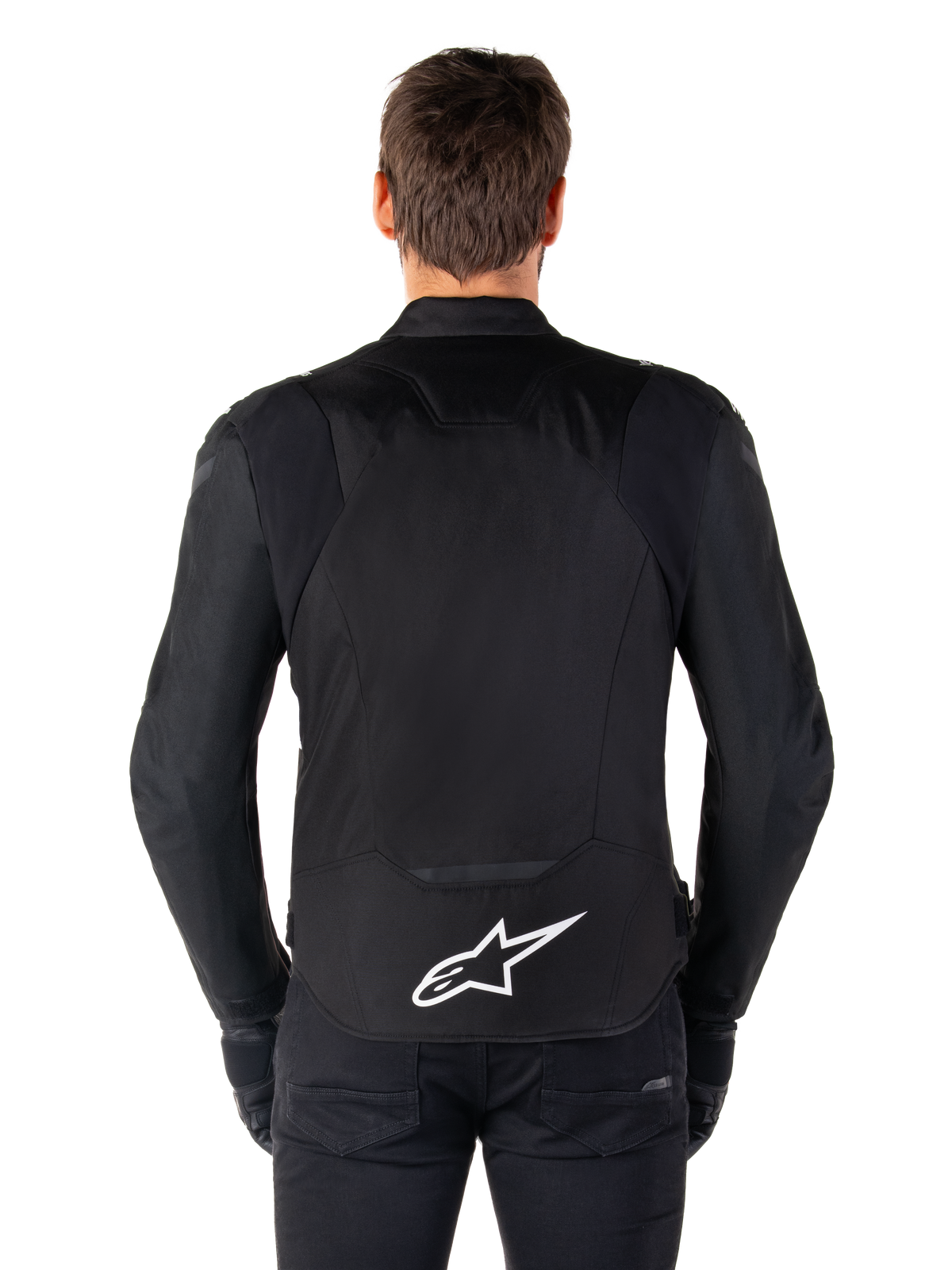 Wodoodporna kurtka Alpinestars T-Jaws V4, czarna kurtka motocyklowa widok od tyłu, białe logo Alpinestars na dolnej części pleców, przedłużony tył dla lepszej osłony, model w czarnych spodniach i rękawicach, sportowy design tekstylny