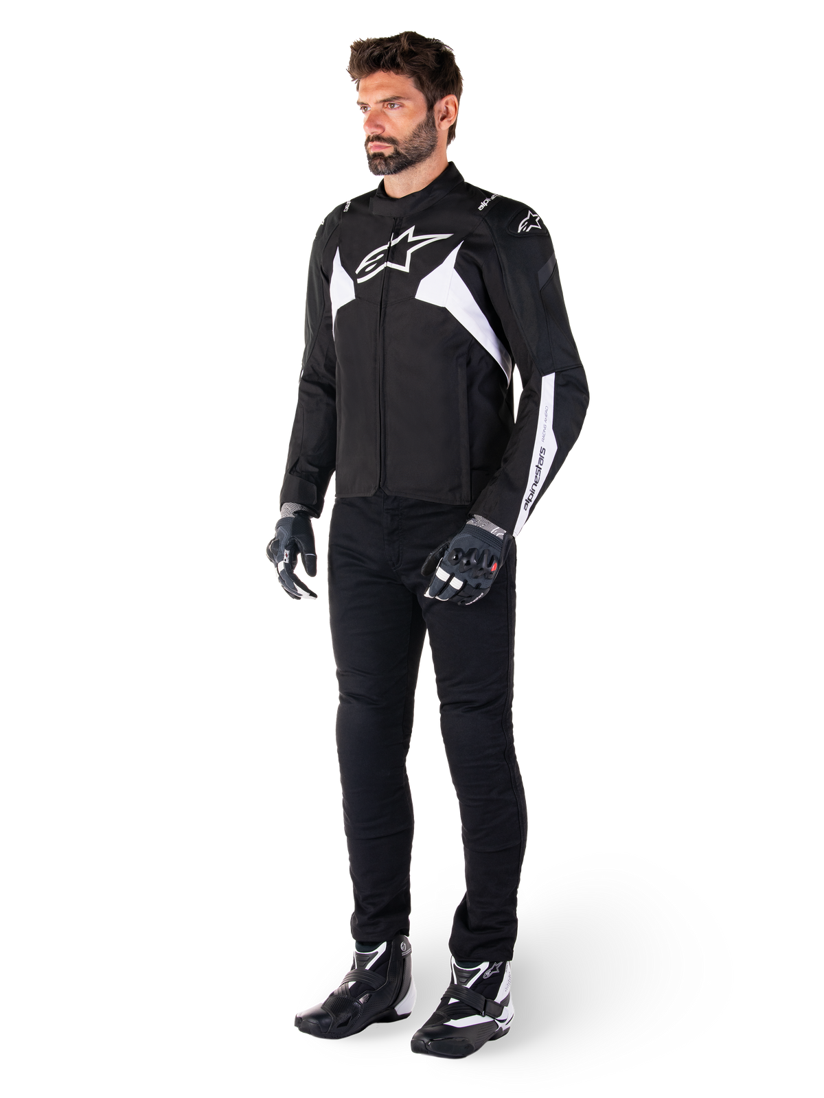 Męski model w kurtce Alpinestars T-Jaws V4 Waterproof w kolorze czarno-białym, sportowa kurtka tekstylna z białym logo gwiazdy i detalami na rękawach, zestawiona z czarnymi spodniami motocyklowymi, rękawicami i butami, tworząca kompletny zestaw do jazdy szosowej.
