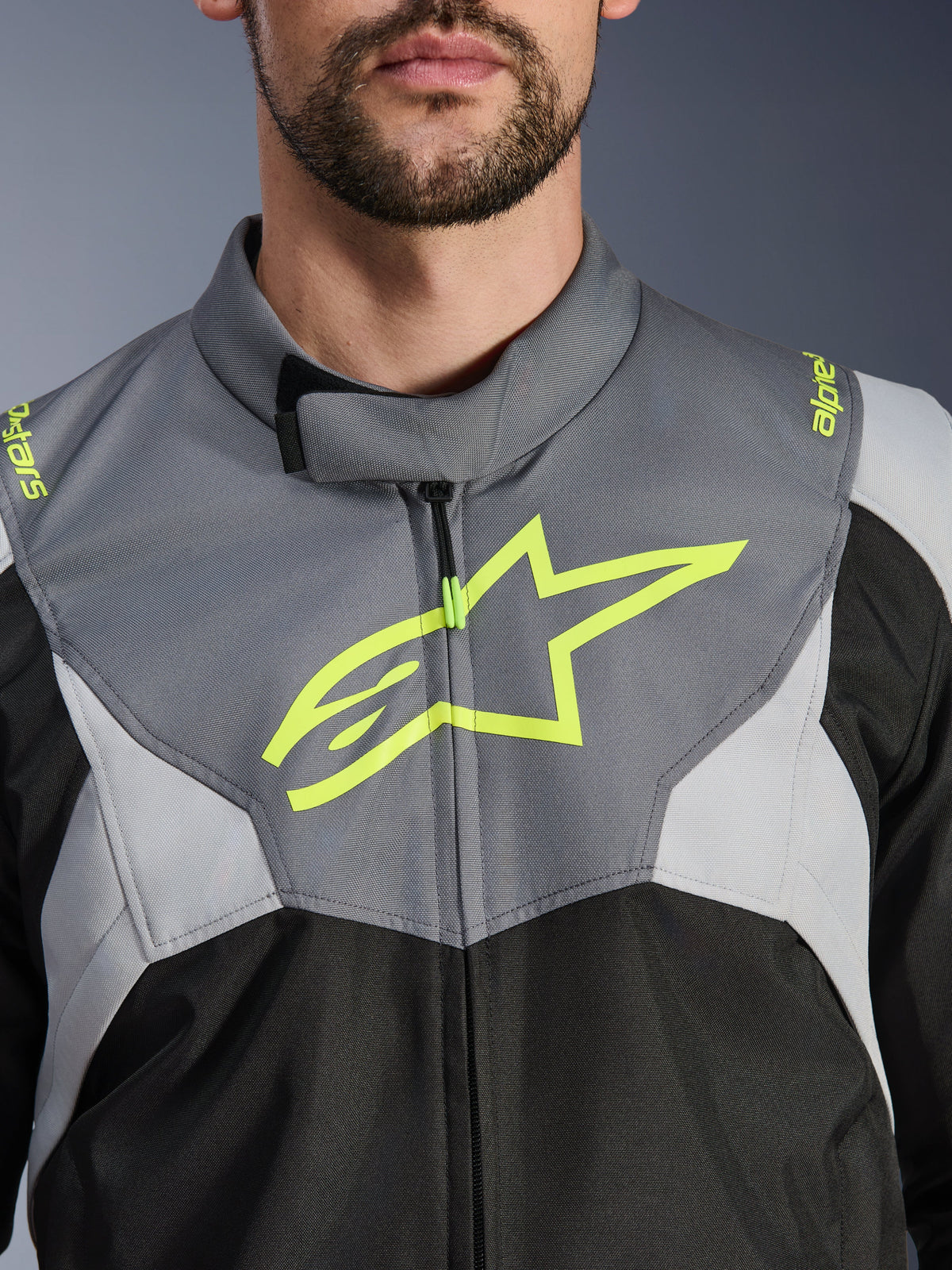 Alpinestars T-Jaws V4 Waterproof Jacket, kolor czarny, jasnoszary i ciemnoszary, zbliżenie na klatkę piersiową i kołnierz, wyraziste neonowożółte logo gwiazdy Alpinestars i branding na ramionach, wytrzymały materiał tekstylny do jazdy motocyklem
