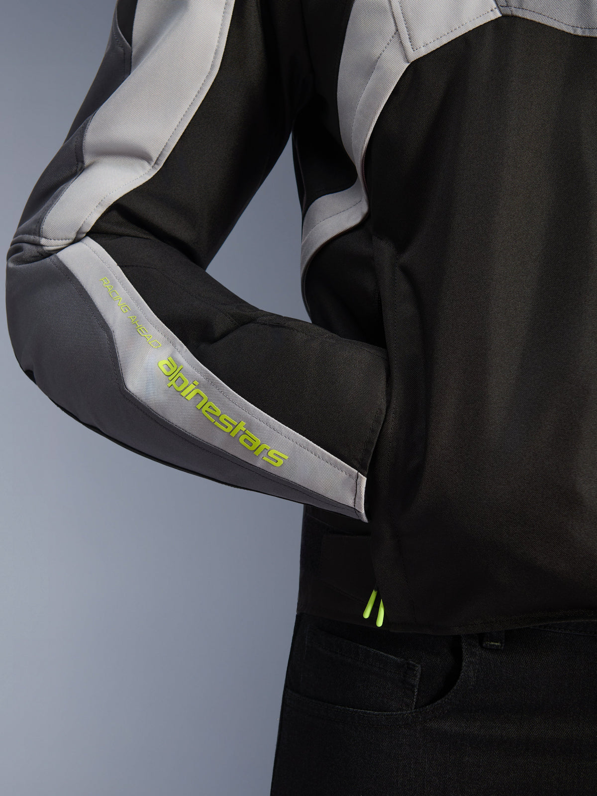 Alpinestars T-Jaws V4 Waterproof Jacket, kurtka motocyklowa, czarna, lodowo-szara i ciemnoszara, zbliżenie na detal rękawa z fluorescencyjnym żółtym brandingiem Alpinestars, materiał tekstylny z boczną kieszenią i wielopanelową konstrukcją