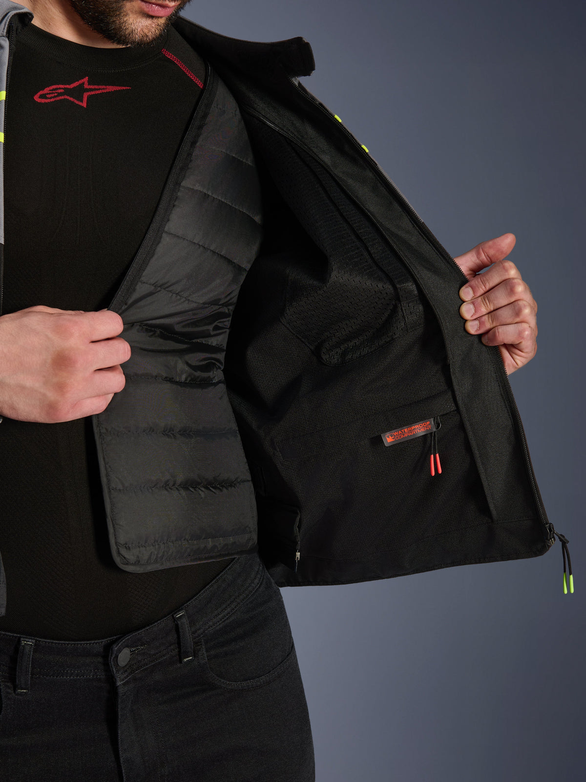 Widok wnętrza kurtki Alpinestars T-Jaws V4 Waterproof, prezentujący wyjmowaną czarną pikowaną podszewkę termiczną i wodoodporną kieszeń wewnętrzną z czerwoną etykietą, siatkowa podszewka, konstrukcja motocyklowa klasy premium.