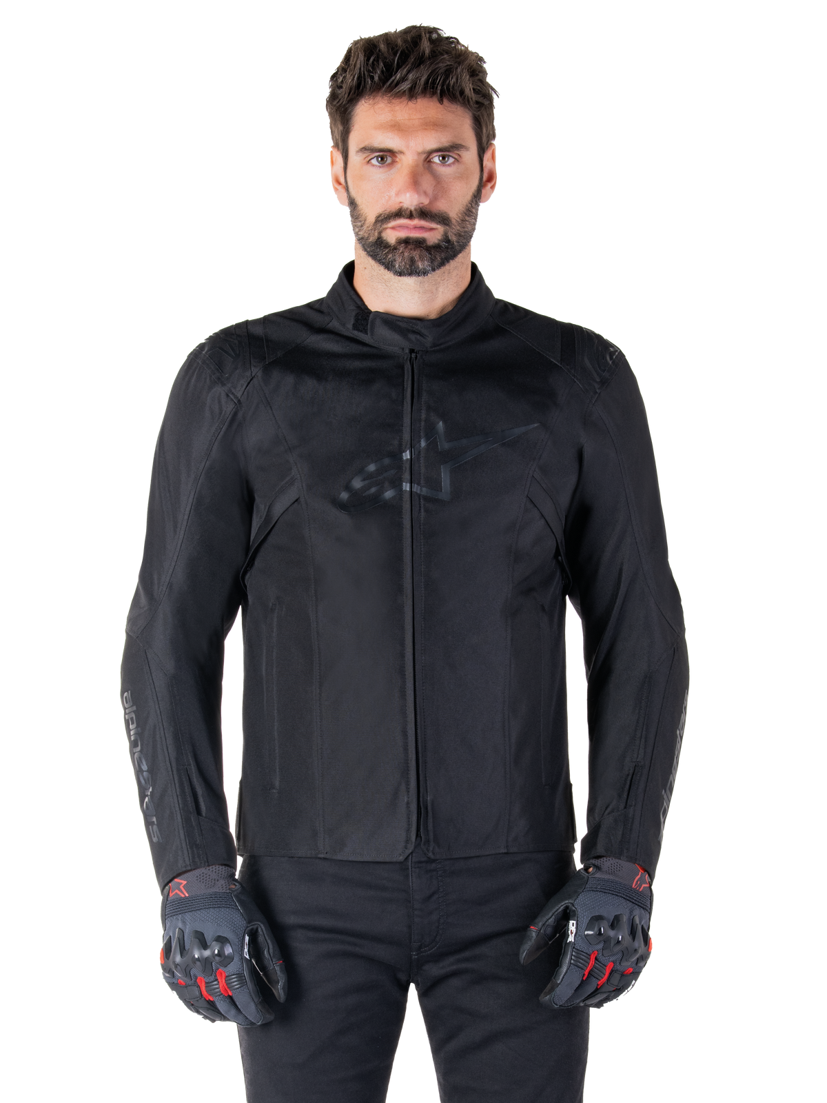 Alpinestars T-SPS V2 Waterproof Jacket, czarna motocyklowa kurtka tekstylna, noszona przez motocyklistę w czarno-czerwonych rękawicach, z wysokim kołnierzem, zamkiem błyskawicznym z przodu i subtelnym logo na klatce piersiowej, wodoodporna ochrona do jazdy sportowej i miejskiej