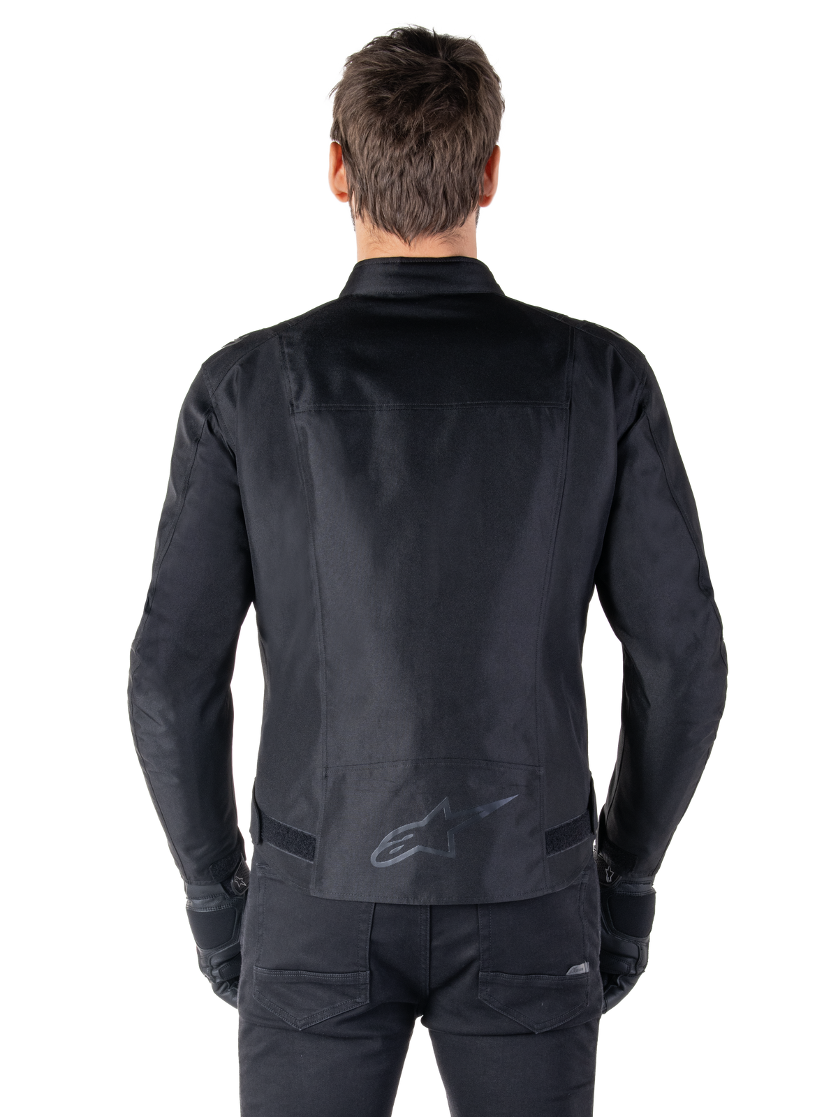 Alpinestars T-SPS V2 Waterproof Jacket, czarna, widok z tyłu ukazujący sportową sylwetkę, odblaskowe logo Alpinestars w dolnej części pleców oraz przedłużony tył dla dodatkowej osłony podczas jazdy