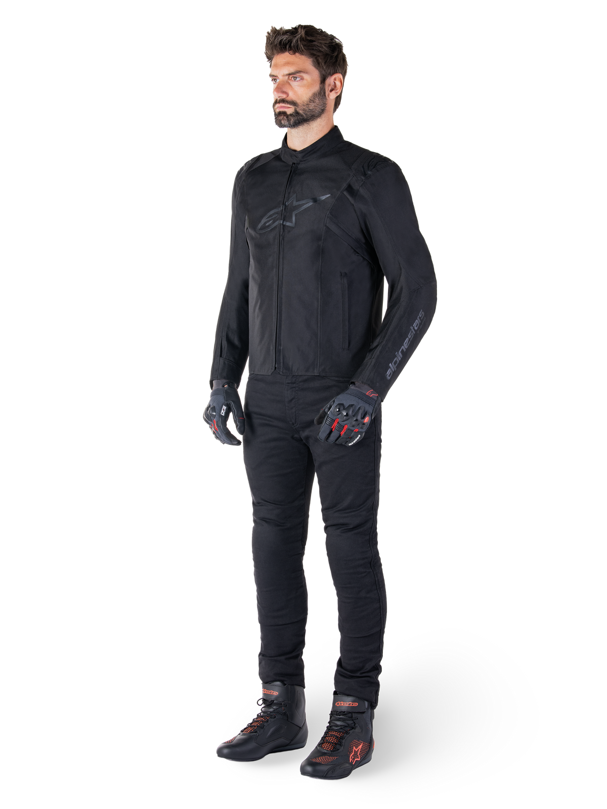 Wodoodporna kurtka Alpinestars T-SPS V2, czarna, prezentowana przez modela w komplecie z czarnymi spodniami, czarnymi rękawicami z czerwonymi akcentami i czarnymi butami motocyklowymi, kompletny ubiór motocyklowy do jazdy miejskiej i sportowej, białe tło