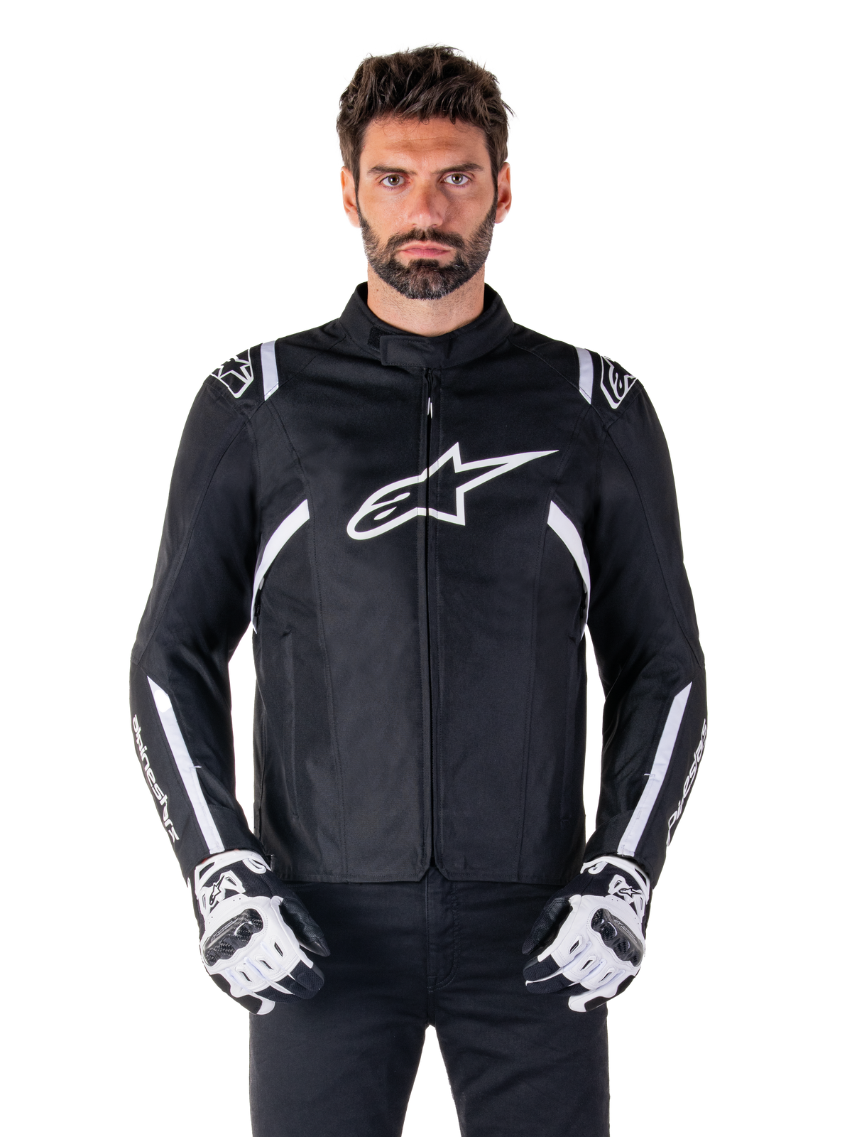 Alpinestars T-SPS V2 Waterproof Jacket w kolorze czarno-białym, widok z przodu na modelu, wodoodporna tekstylna kurtka motocyklowa z białymi pasami na ramionach i rękawach, duże białe logo Alpinestars na piersi, noszona z ochronnymi rękawicami motocyklowymi, smukła sylwetka inspirowana sportem