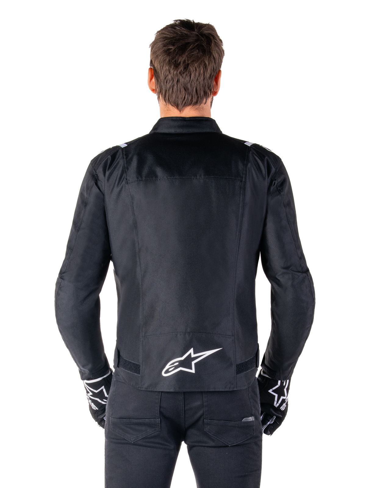 Alpinestars T-SPS V2 Waterproof Jacket, czarno-biała, widok z tyłu z białym logo Alpinestars na dole pleców, zestaw z czarnymi spodniami i rękawicami, tekstylna kurtka motocyklowa o sportowym kroju