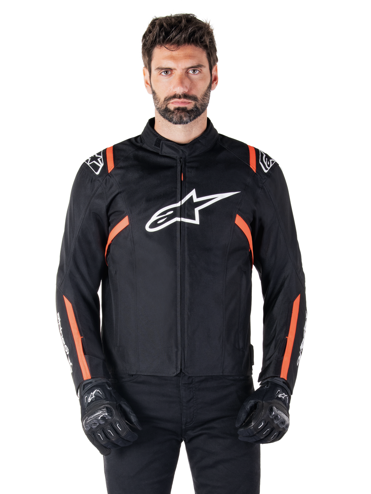 Wodoodporna kurtka Alpinestars T-SPS V2, w kolorze czarnym, białym i czerwonym (Red Fluo), prezentowana przez modela w czarnych rękawicach motocyklowych, z dużym białym logo Alpinestars na klatce piersiowej i jaskrawymi pomarańczowymi akcentami na ramionach i rękawach.