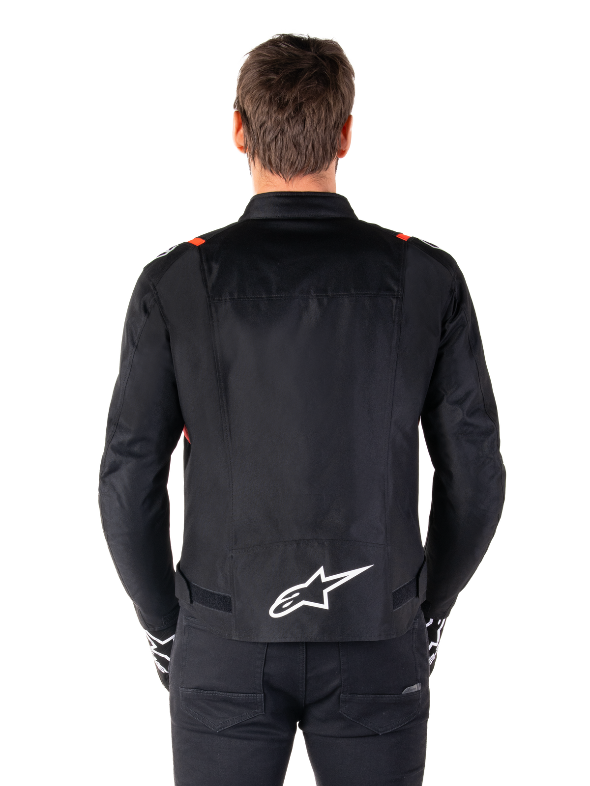 Alpinestars T-SPS V2 Waterproof Jacket, czarna z białymi i czerwonymi akcentami Fluo, widok z tyłu z dużym białym logo Alpinestars na dole pleców, tekstylna kurtka motocyklowa o sportowym kroju, noszona z czarnymi spodniami i rękawicami