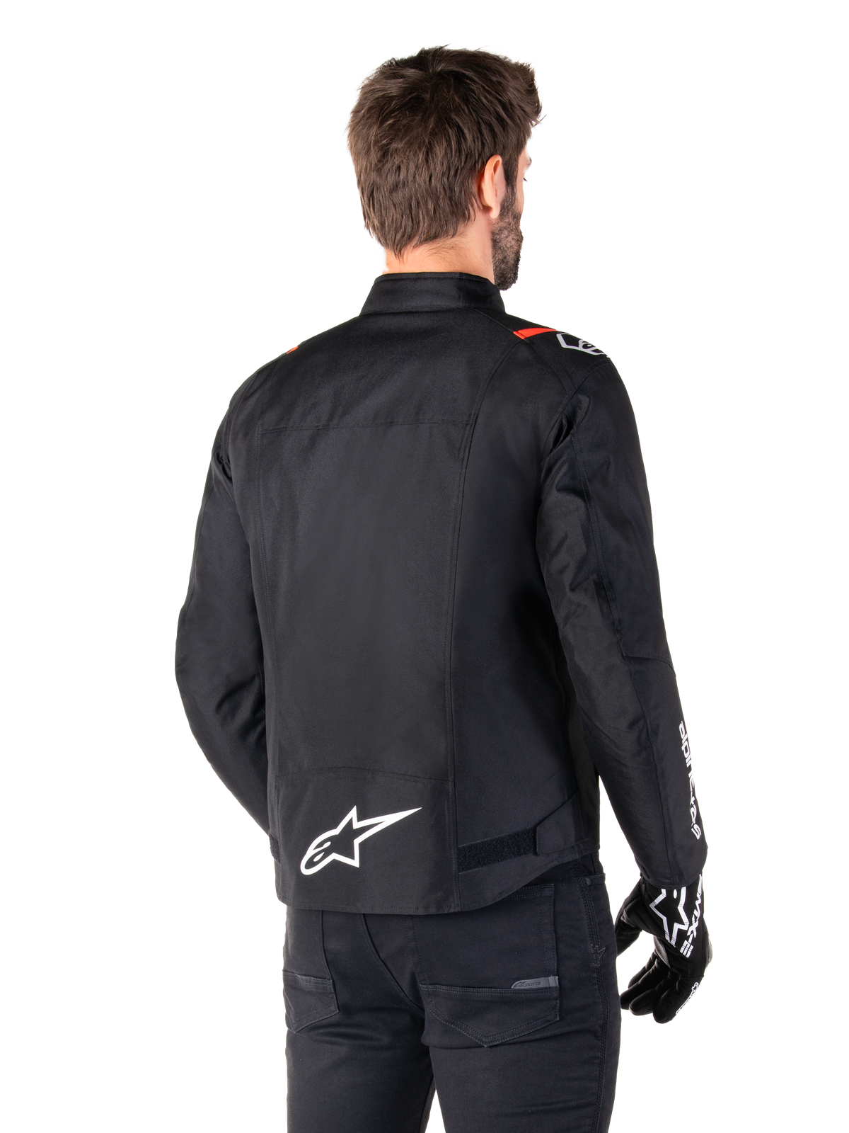 Kurtka Alpinestars T-SPS V2 Waterproof, Black White Red Fluo, widok z tyłu, białe logo Alpinestars w dolnej części pleców i czerwone akcenty na ramionach, zestawiona z czarnymi rękawicami i spodniami, sportowa tekstylna kurtka motocyklowa