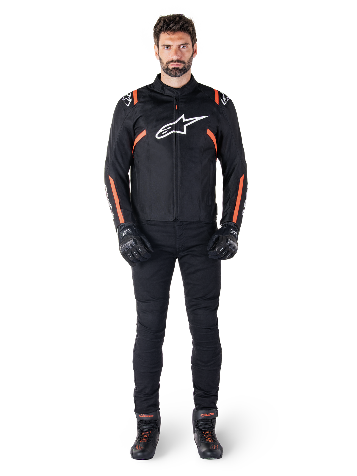 Męski model ubrany w kurtkę Alpinestars T-SPS V2 Waterproof Jacket w kolorystyce Black White Red Fluo, zestawioną z czarnymi spodniami i rękawicami motocyklowymi, z białym logo Alpinestars na piersi i czerwonymi akcentami na rękawach.