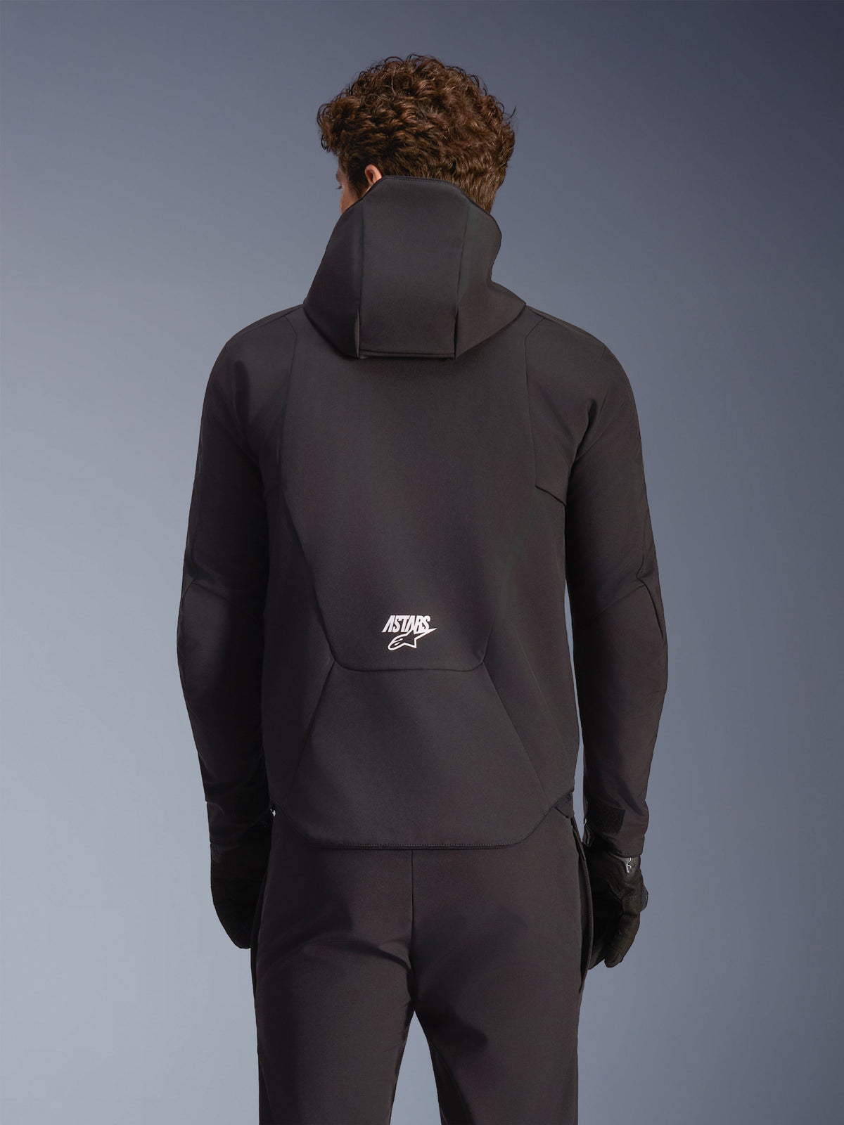 Alpinestars Kurtka Aeroshell Wodoodporna, czarna męska kurtka motocyklowa softshell z kapturem, widok z tyłu na modelu z białym logo.