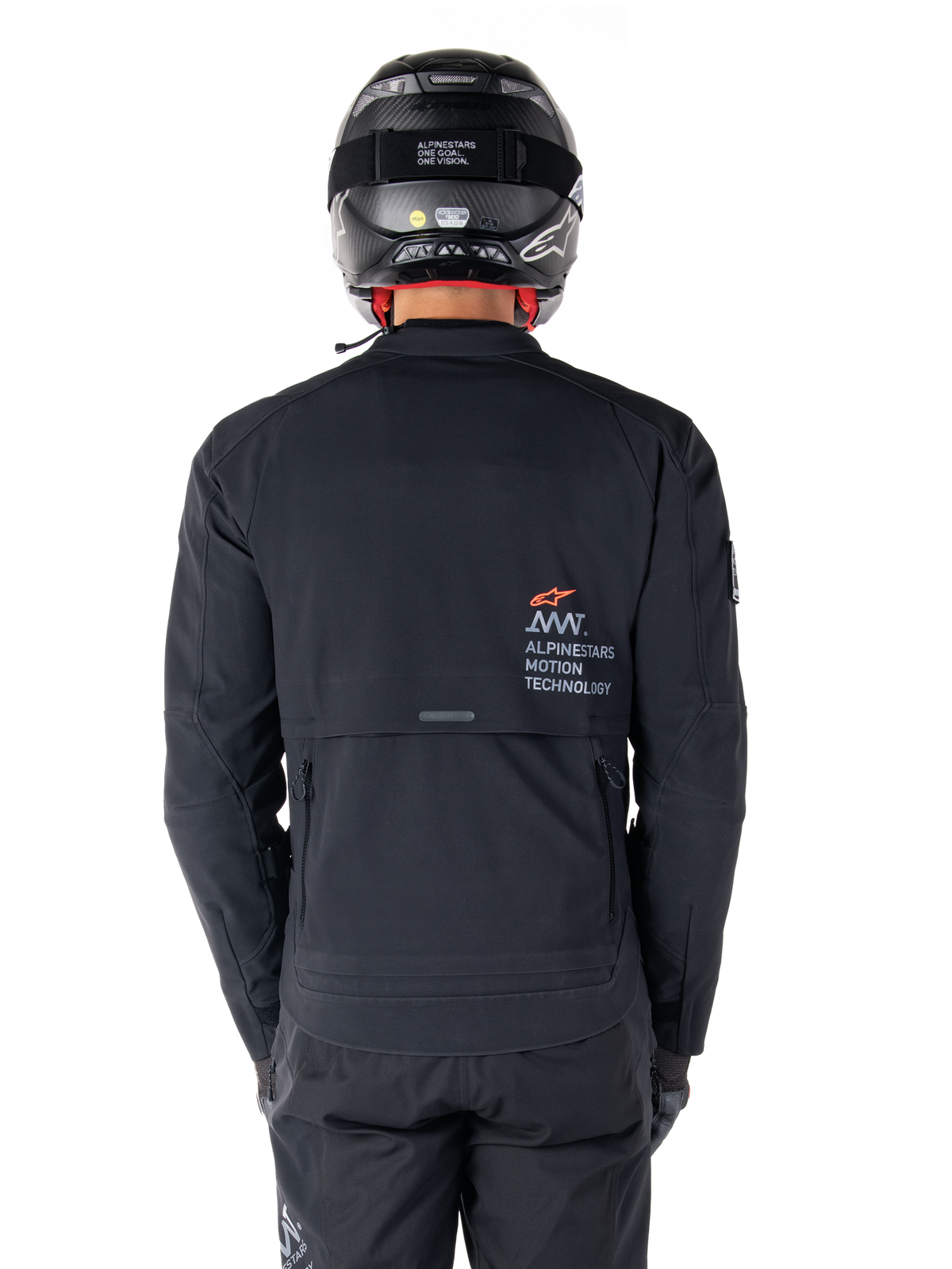 Kurtka Alpinestars AMT-8 Stretch Drystar® XF, widok z tyłu, czarna, noszona z czarnym kaskiem i spodniami, z logo Alpinestars Motion Technology na plecach, design adventure touring z ergonomicznego elastycznego materiału.