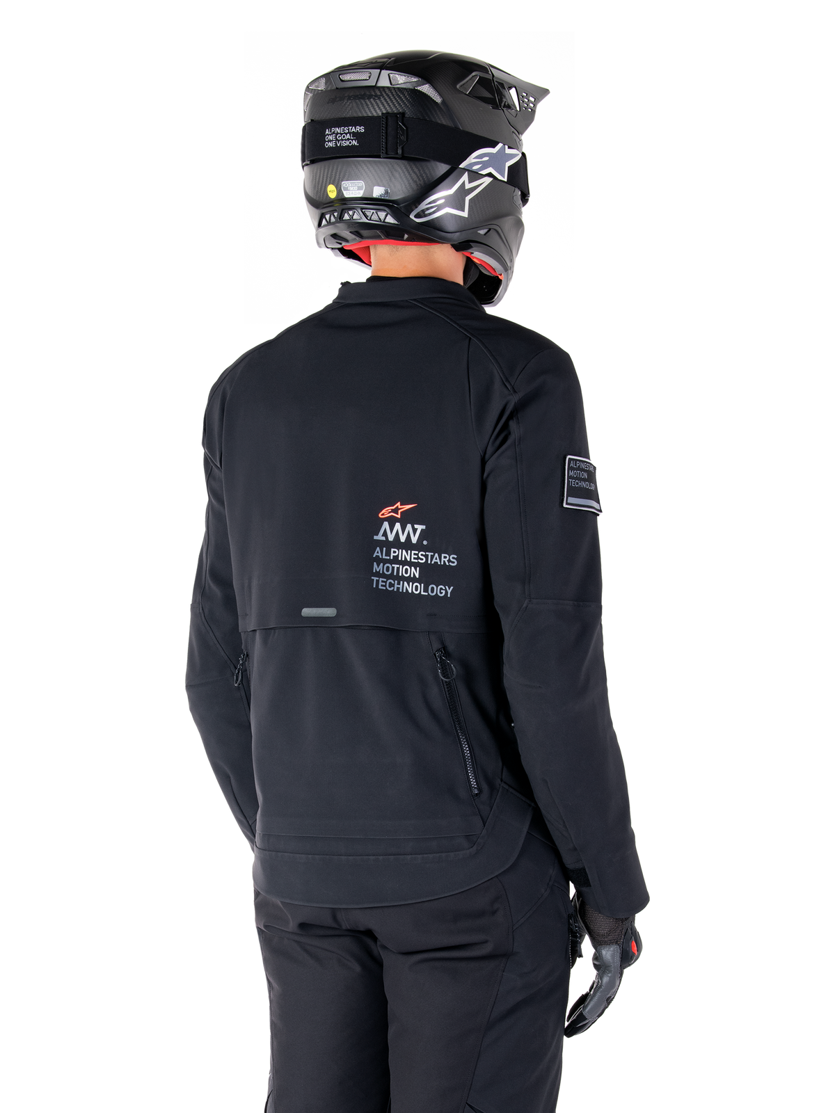 Widok z tyłu motocyklisty w czarnej kurtce Alpinestars AMT-8 Stretch Drystar® XF, z logo „AMT Alpinestars Motion Technology” na plecach, techniczną wentylacją na zamki, w czarnym kasku motocyklowym i rękawicach