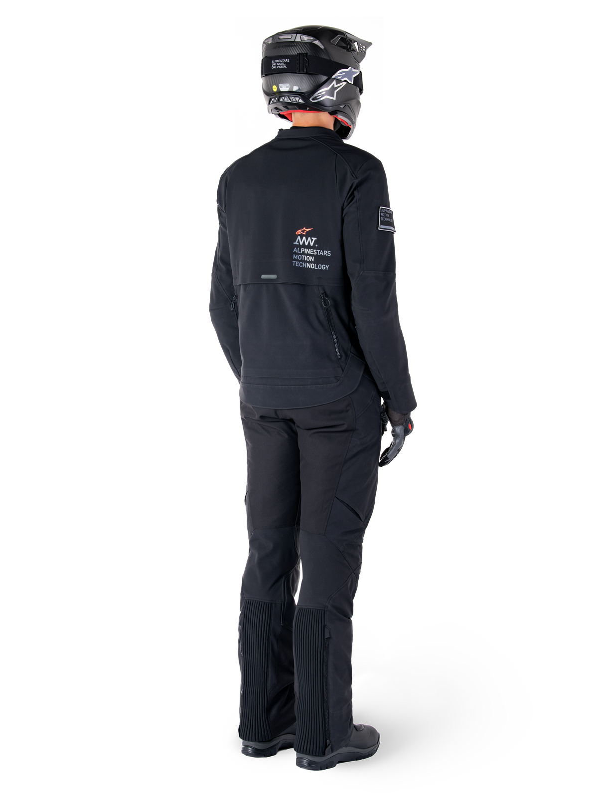 Kurtka Alpinestars AMT-8 Stretch Drystar® XF, czarna, widok z tyłu motocyklisty ubranego w kurtkę, pasujące czarne spodnie i czarny kask, z logo „Alpinestars Motion Technology” na plecach, techniczny elastyczny materiał do jazdy motocyklowej typu adventure