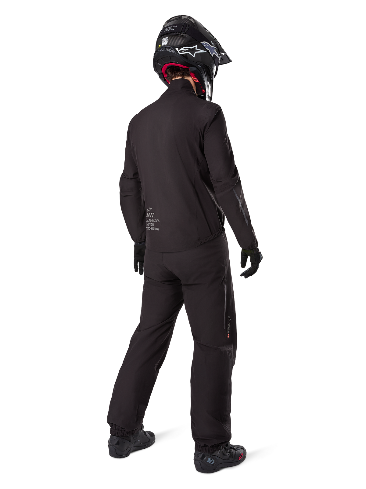 Widok z tyłu motocyklisty w podpince kurtki Alpinestars AMT-8 Stretch Drystar® XF, czarna techniczna odzież motocyklowa, noszona z pasującymi spodniami i czarnym kaskiem, logo „AMT Alpinestars Motion Technology” na plecach, minimalistyczny design do turystyki przygodowej