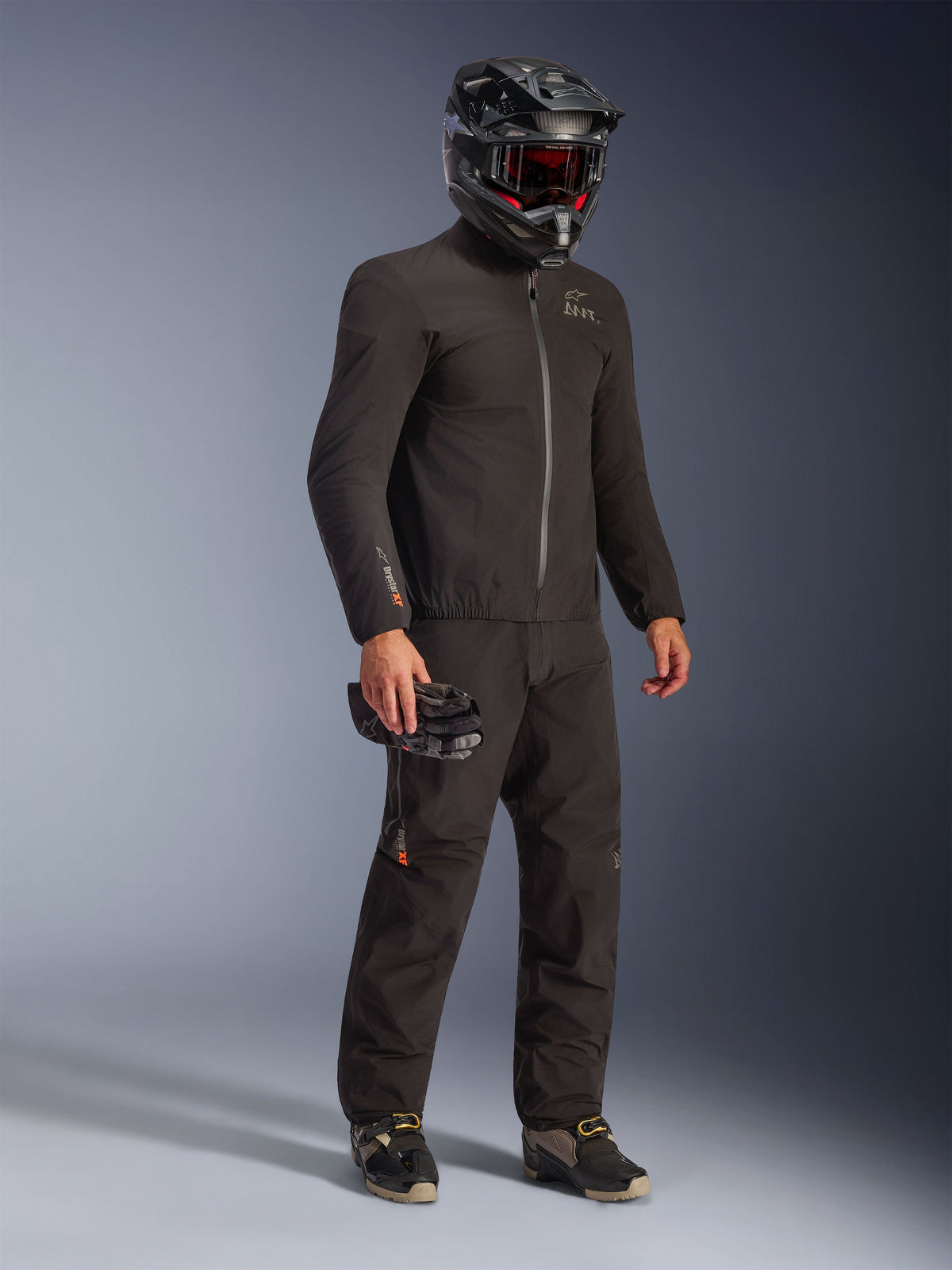 Alpinestars AMT-8 Stretch Drystar® XF Jacket in Black, worn as part of a full riding kit with matching pants and a black helmet, featuring a sleek textile design with orange Drystar XF branding on the sleeve, ideal for adventure touring.