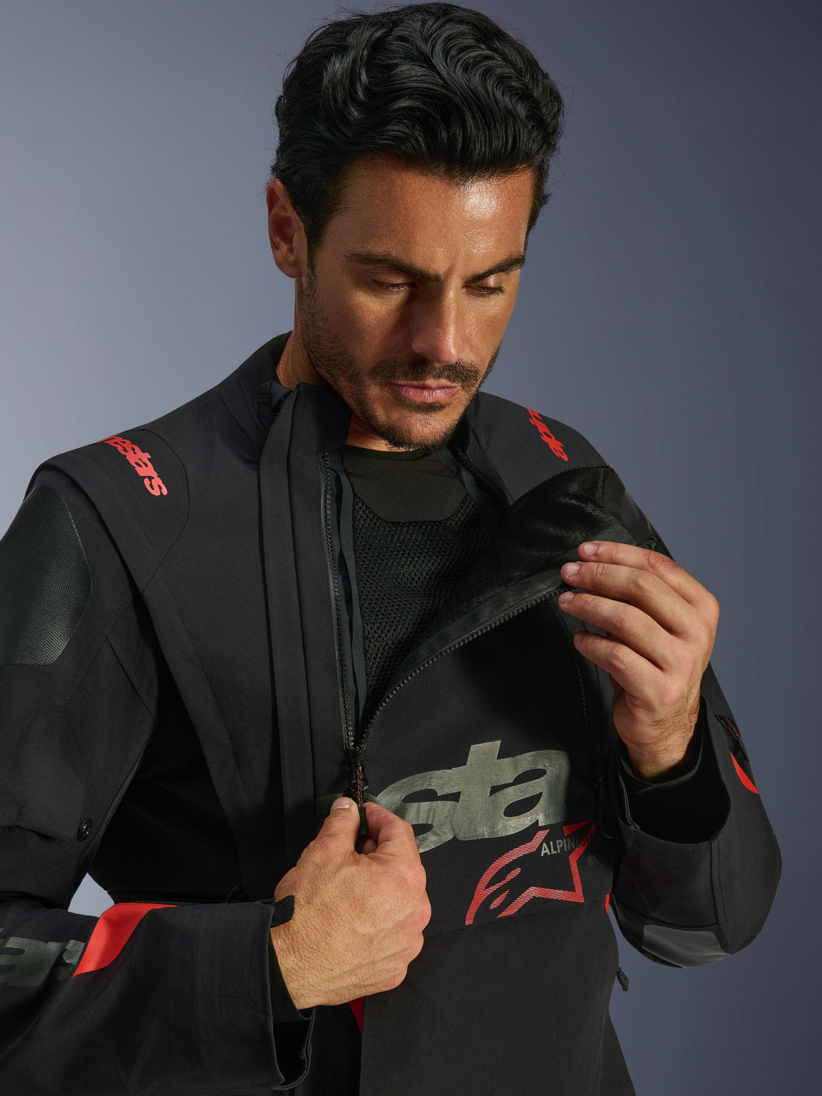 Kurtka Alpinestars Halo Pro Drystar® XF Laminated Jacket, Black Dark Shadow, model prezentujący modułowy system wentylacji poprzez rozpięcie asymetrycznego przedniego panelu na klatce piersiowej, kurtka typu adventure touring z czerwonym brandingiem Alpinestars i technicznymi detalami z siatki