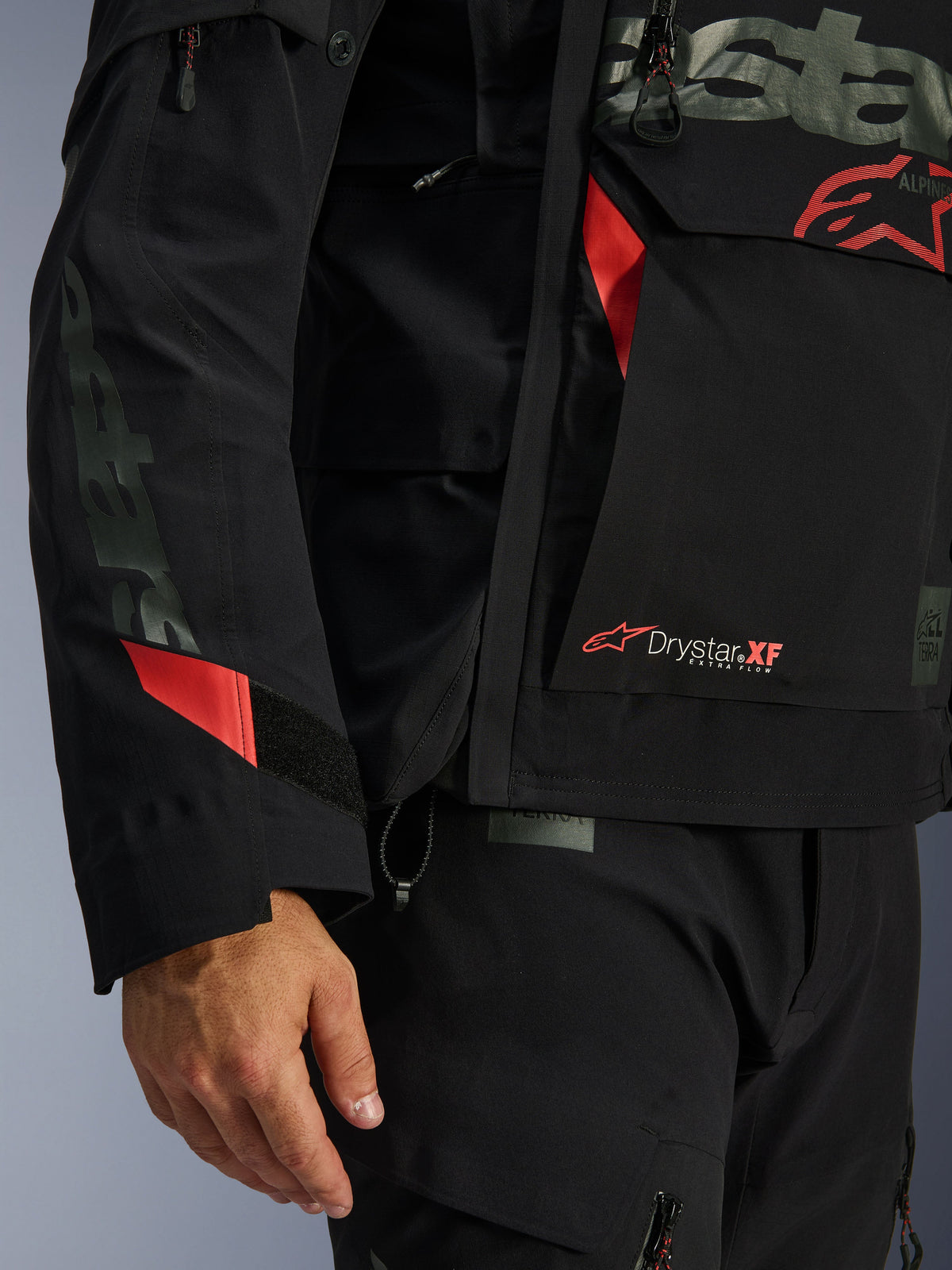 Alpinestars Halo Pro Drystar® XF Laminated Jacket, kurtka motocyklowa, czarna z czerwonymi akcentami, zbliżenie na branding Drystar® XF, techniczna tekstura laminowanej powłoki oraz regulowane detale rękawów do jazdy adventure