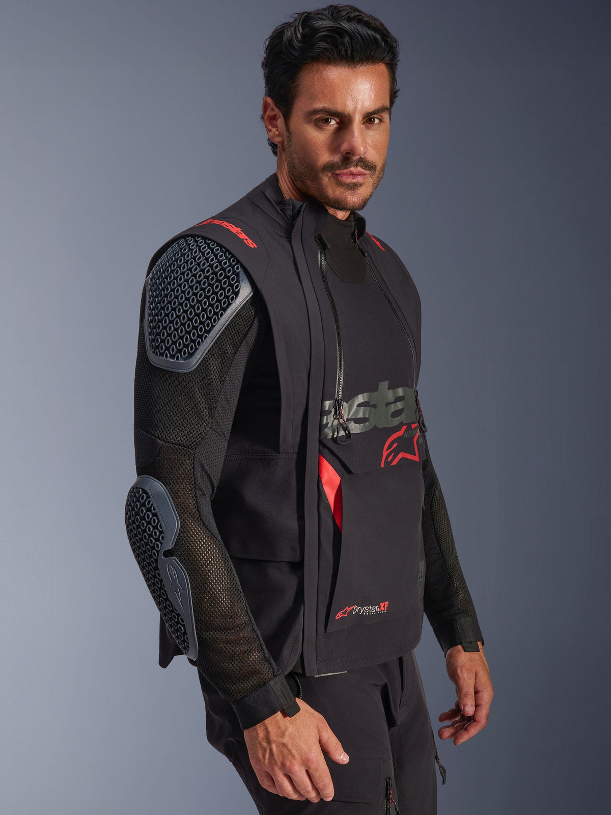 Laminowana kurtka Alpinestars Halo Pro Drystar® XF, czarna i Dark Shadow, kurtka motocyklowa adventure prezentowana na modelu, modułowa konfiguracja z siatkowymi rękawami i zintegrowanymi ochraniaczami ramion i łokci, czerwone akcenty logo i techniczne wodoodporne zamki