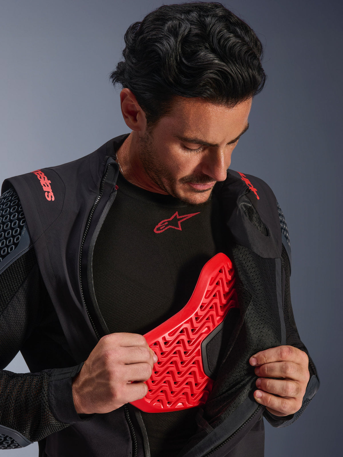 Kurtka laminowana Alpinestars Halo Pro Drystar® XF w kolorze Black Dark Shadow, noszona przez modela i rozpięta, aby odsłonić czerwony ochraniacz klatki piersiowej Nucleon Flex Pro, techniczna kurtka motocyklowa, odzież do jazdy adventure