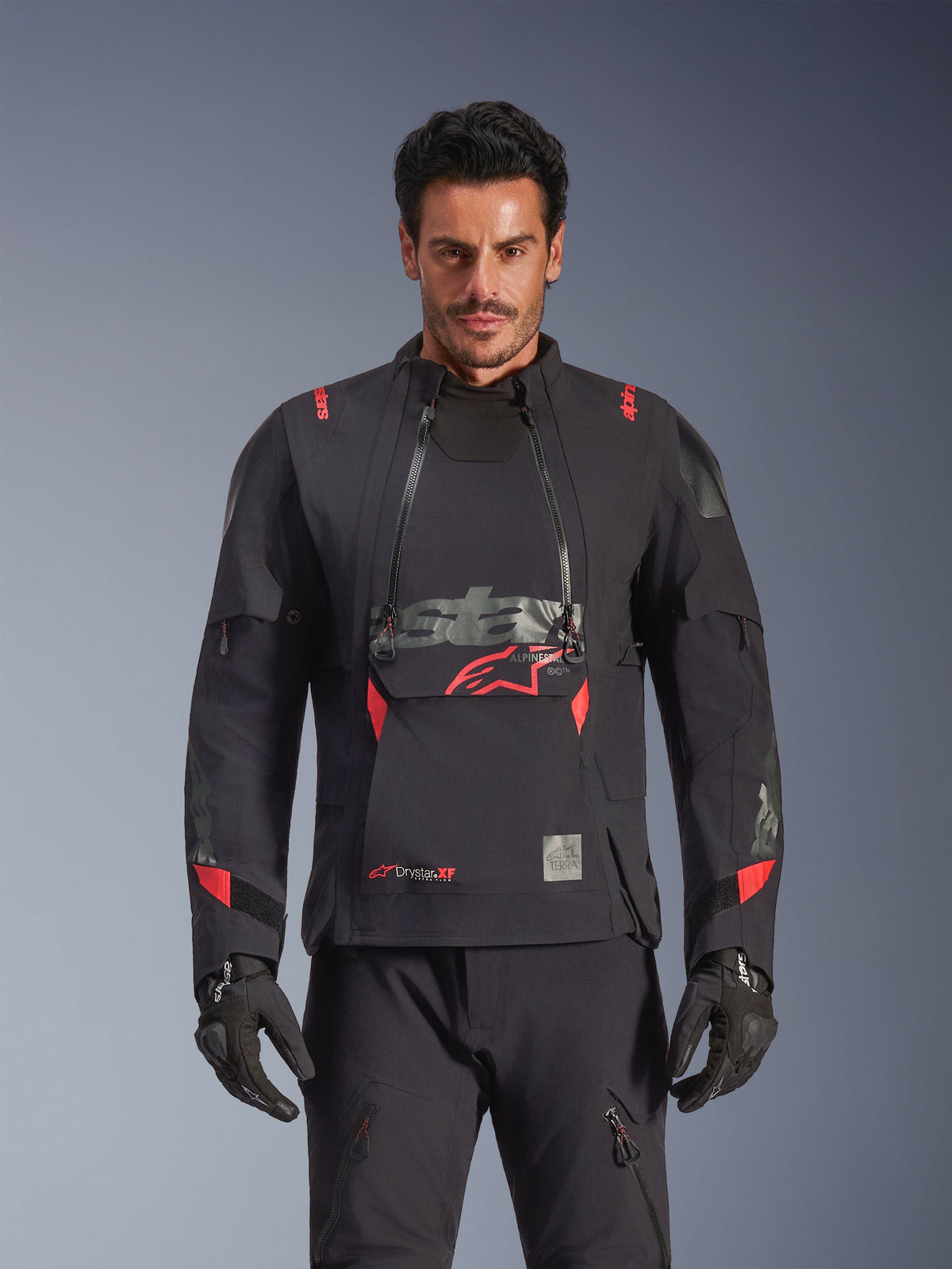 Alpinestars Halo Pro Drystar® XF Laminated Jacket, kurtka motocyklowa adventure, czarna (Dark Shadow) z czerwonymi akcentami, męski model w pełnym stroju technicznym z pasującymi rękawicami i spodniami, widok z przodu ukazujący modułowe panele wentylacyjne na klatce piersiowej i wodoodporną konstrukcję