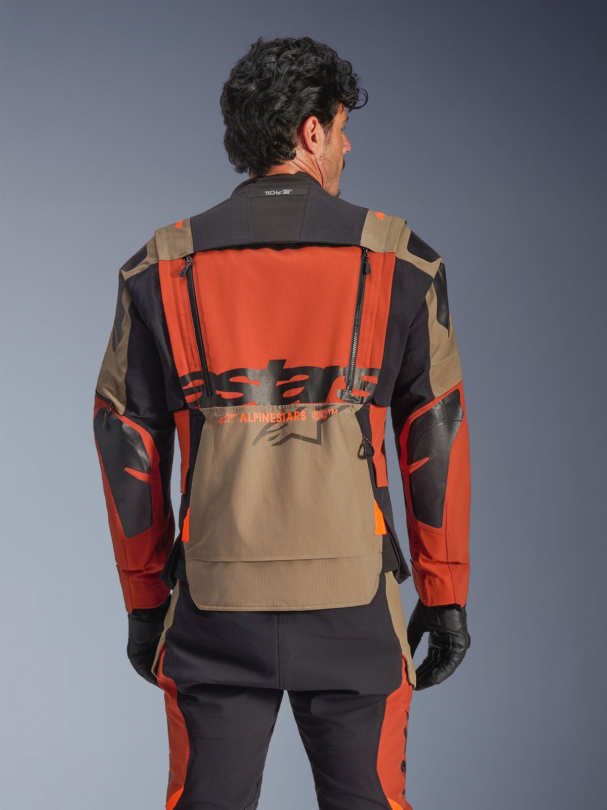 Kurtka Alpinestars Halo Pro Drystar® XF Laminated Jacket, kolorystyka Walnut Rust Black, widok z tyłu, duży pomarańczowy panel na plecach z czarnym brandingiem ASTARS, dolna kieszeń w kolorze walnut, kołnierz Tech-Air® Ready, noszona z pasującymi spodniami typu adventure i czarnymi rękawicami