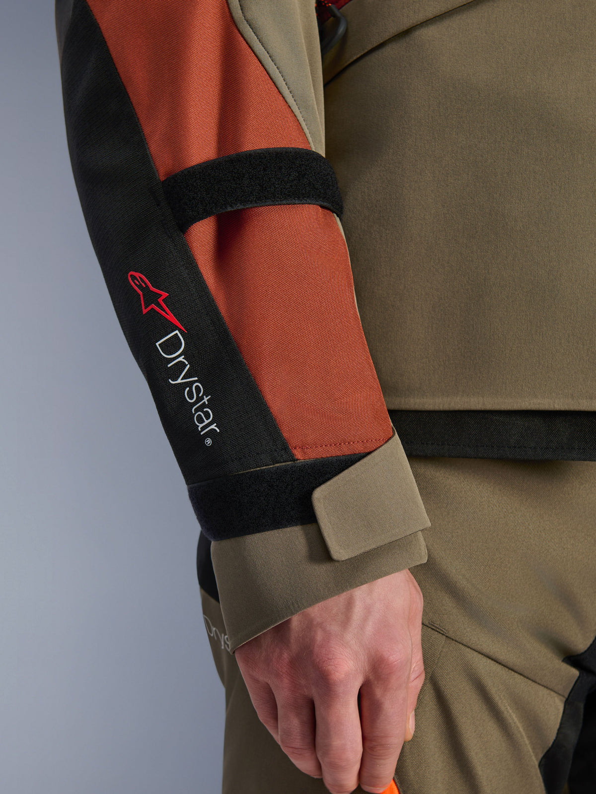 Kurtka Alpinestars Andes V4 Drystar®, kurtka motocyklowa, Walnut Rust Black, zbliżenie na rękaw z brandingiem Drystar® i czerwonym logo gwiazdy, regulowane paski na rzepy na przedramieniu i nadgarstku, wytrzymała tekstylna konstrukcja adventure touring