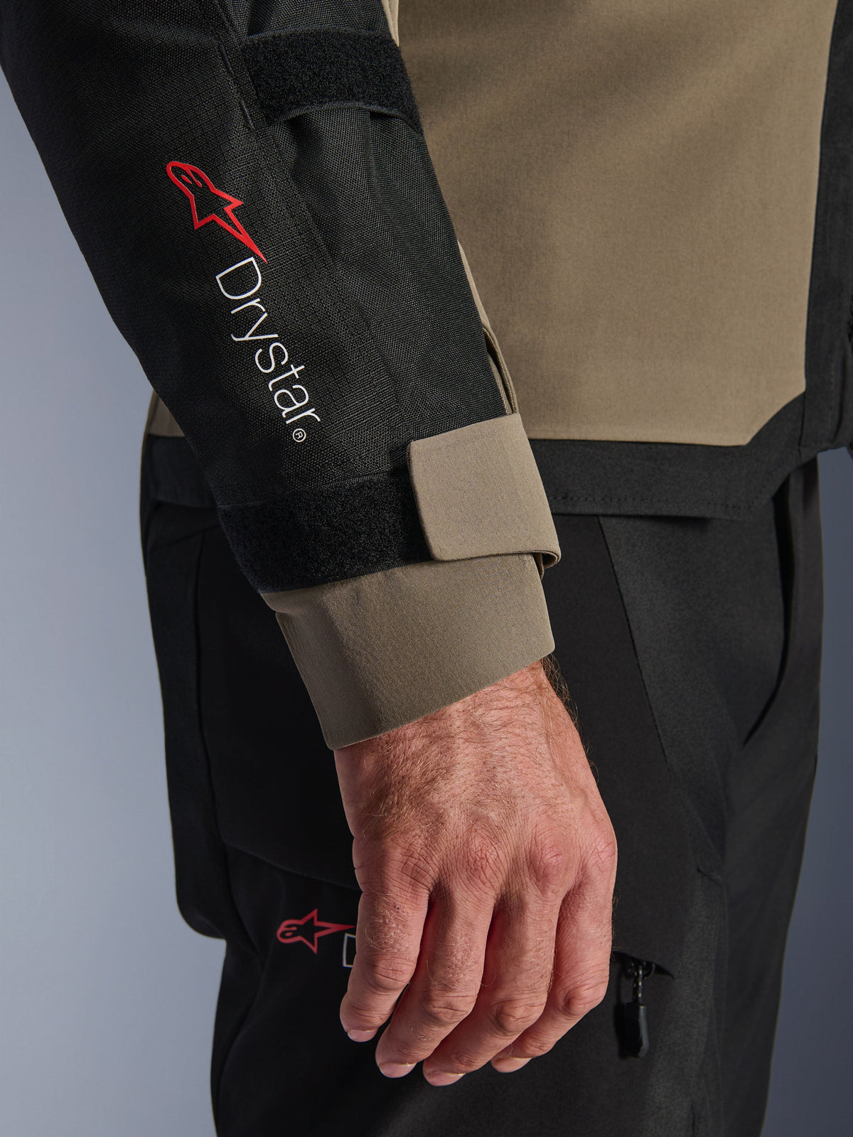 Zbliżenie na kurtkę Alpinestars Andes V4 Drystar® w kolorze Walnut i czarnym, z czerwonym logo Drystar® na przedramieniu i regulowanym paskiem mankietu, część technicznego stroju motocyklowego adventure.