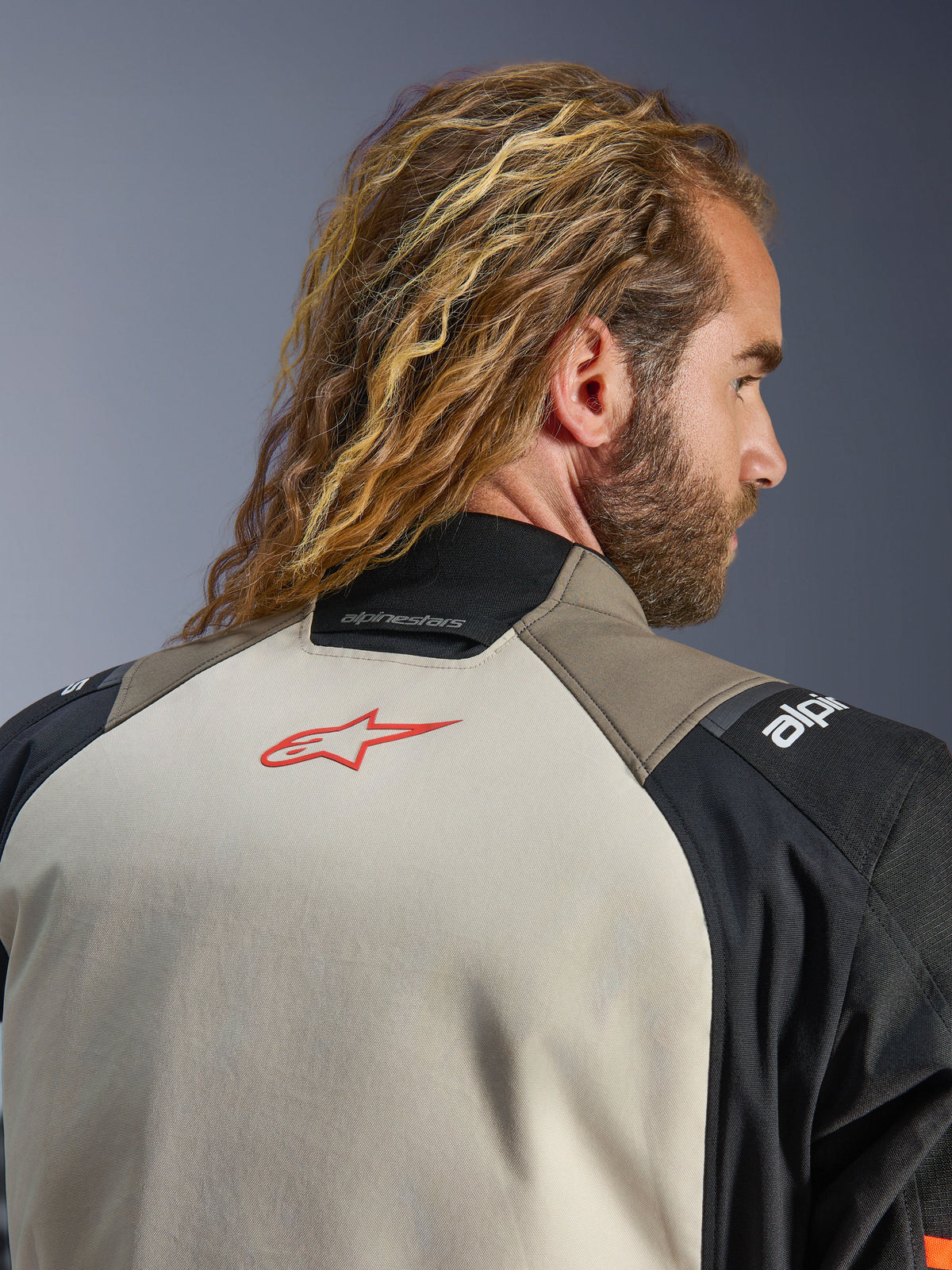 Kurtka Alpinestars Andes V4 Drystar®, wersja kolorystyczna Walnut Mastic Black, zbliżenie na górną część pleców i kołnierz, czerwone logo gwiazdy na panelu mastic, tekstylna konstrukcja w kolorach walnut i czarnym, turystyczna odzież motocyklowa adventure