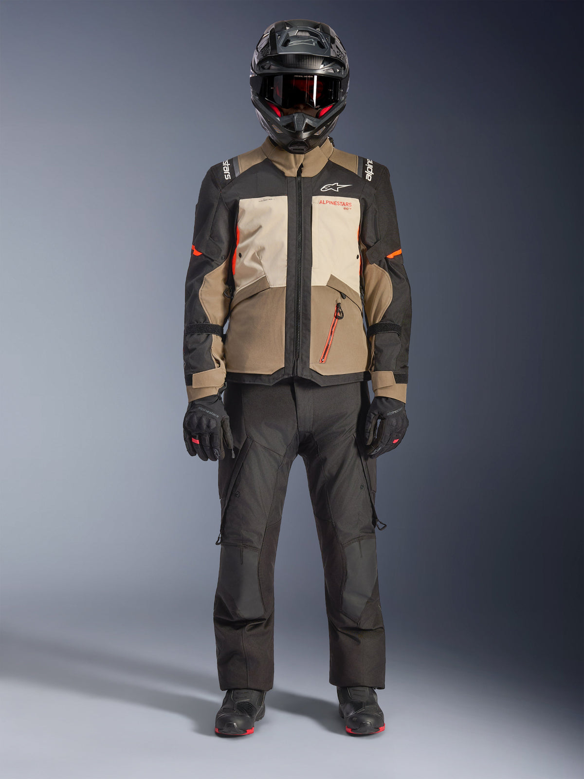 Alpinestars Andes V4 Drystar® Jacket, Walnut Mastic Black, motocyklowa kurtka adventure touring z beżowymi i kremowymi panelami oraz pomarańczowymi akcentami, noszona przez motocyklistę w czarnym kasku adventure, czarnych spodniach i butach, widok całej sylwetki w studio