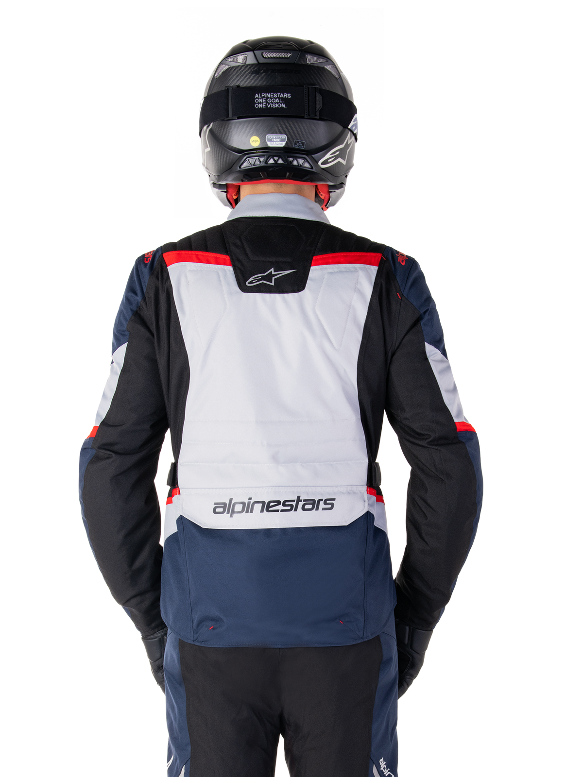 Wodoodporna kurtka Alpinestars ST-1, ciemnoniebieska, czarna z jaskrawoczerwonymi elementami, widok z tyłu prezentujący jasnoszary panel na plecach i logo marki, motocyklowa kurtka adventure touring noszona z czarnym kaskiem i rękawicami, smukła konstrukcja do jazdy w każdych warunkach pogodowych