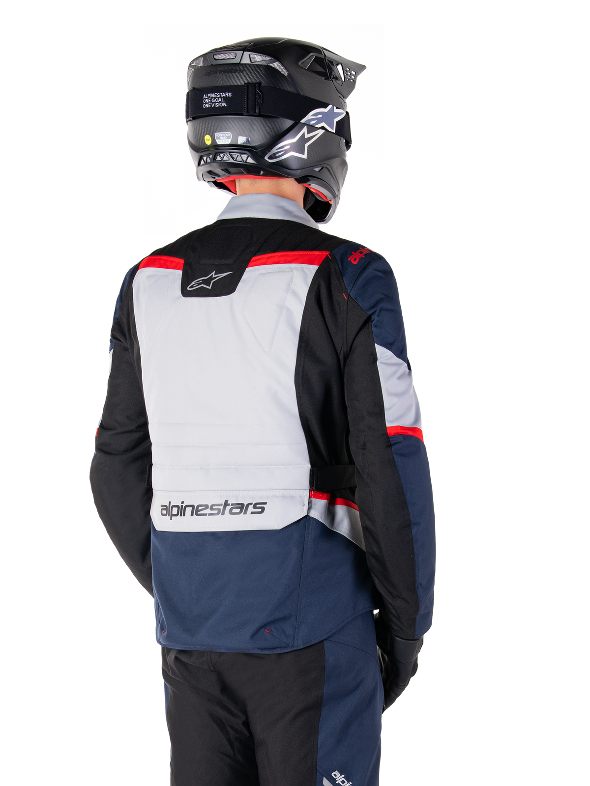Kurtka Alpinestars ST-1 Waterproof, ciemnoniebieska, czarna i jaskrawoczerwona, widok z tyłu na motocyklistę w czarnym kasku adventure, jasnoszare panele i branding Alpinestars, odzież motocyklowa adventure touring