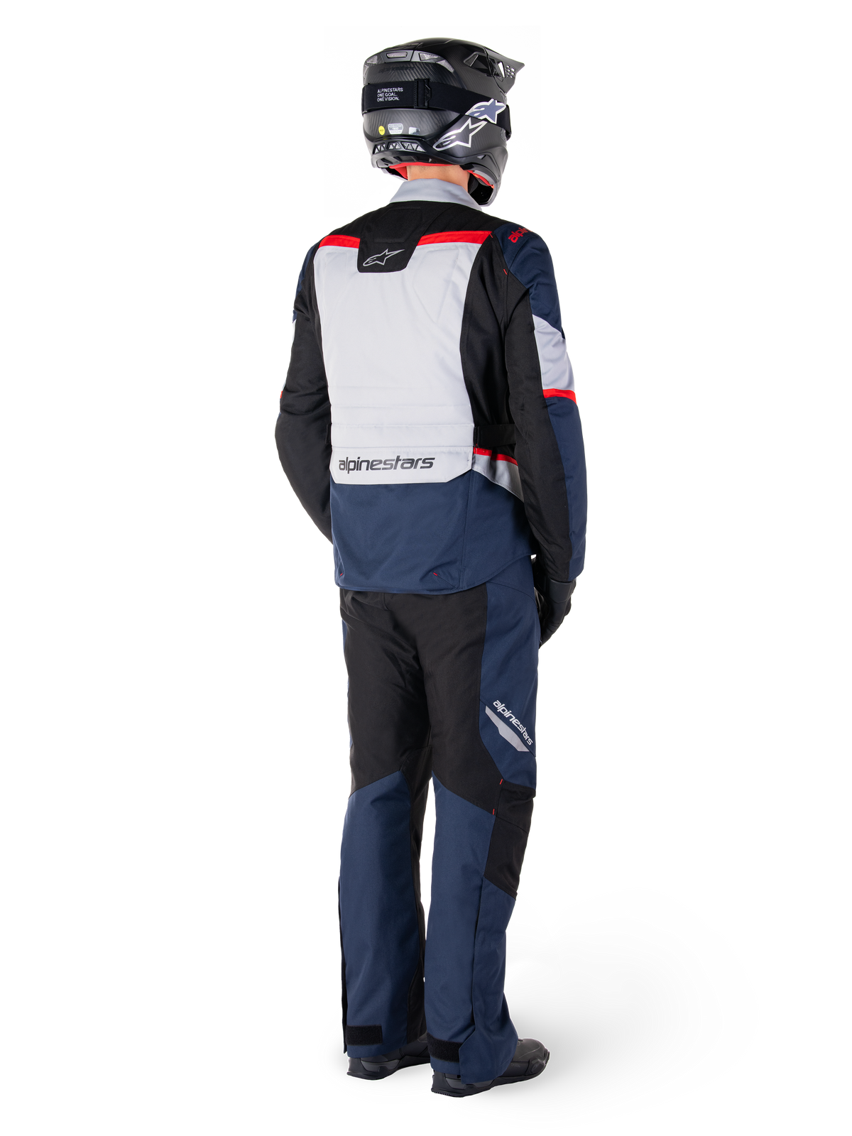 Widok z tyłu motocyklisty ubranego w kurtkę Alpinestars ST-1 Waterproof Jacket w kolorze granatowo-czarno-czerwonym, w zestawie z pasującymi spodniami wodoodpornymi i czarnym kaskiem; widoczny szary panel na plecach z logo Alpinestars oraz design typu adventure touring.