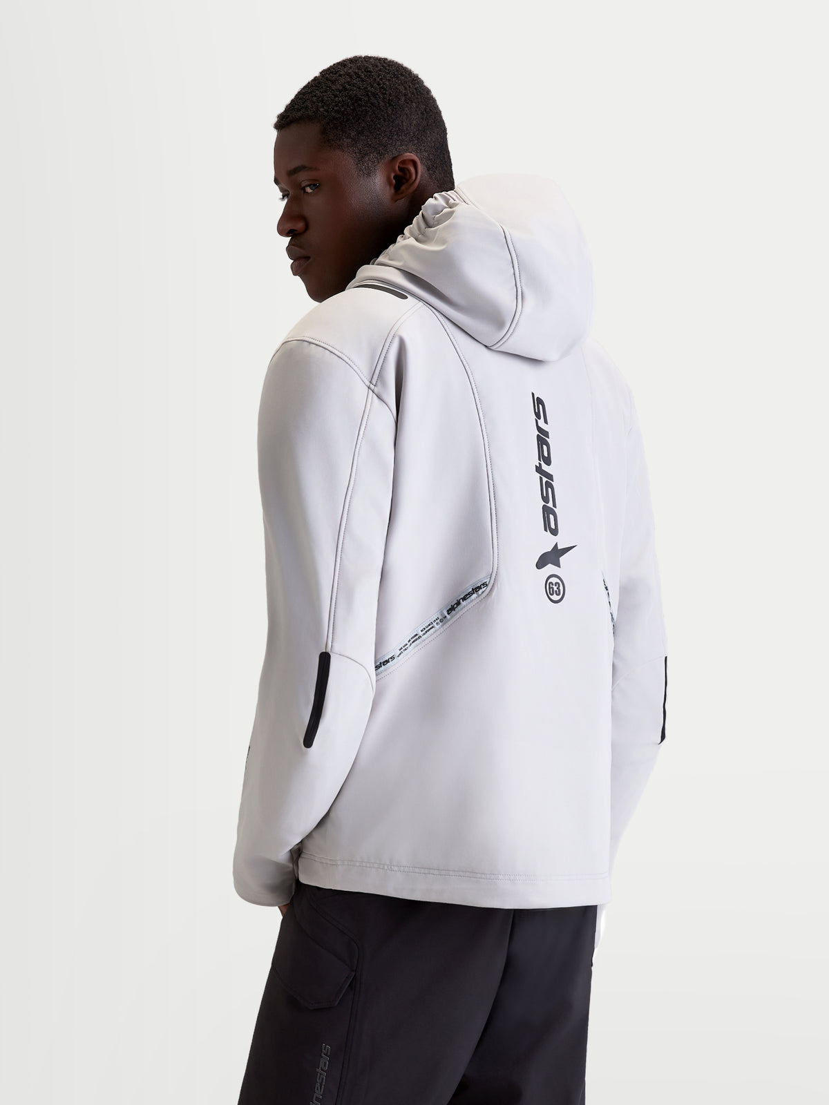 Alpinestars C 5 Drystar kurtka motocyklowa miejska męska w kolorze jasnoszarym i czarnym, widok z tyłu na modelu prezentujący zintegrowany kaptur, konstrukcję softshell oraz pionowe detale z logo na plecach