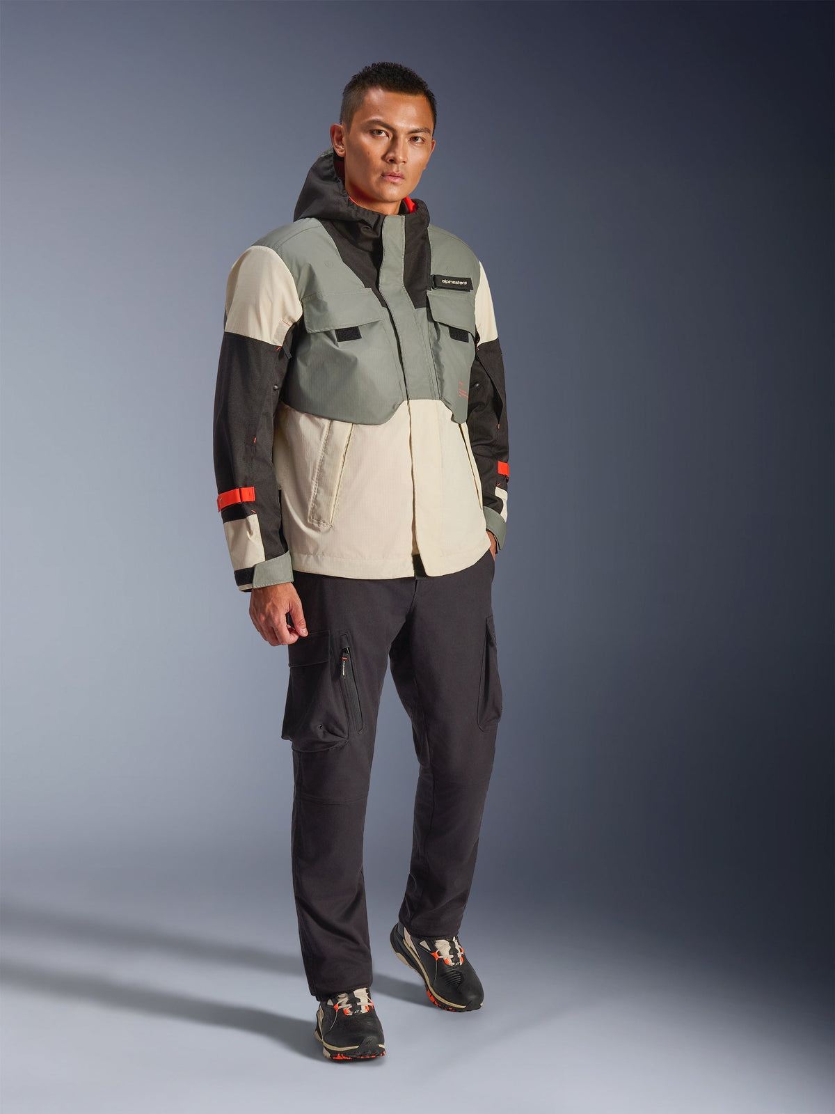 Kurtka wodoodporna Alpinestars Mospher w kolorze Fur Gray Black Ice, wielokolorowa techniczna parka motocyklowa z szarymi, czarnymi i kremowymi panelami oraz czerwonymi akcentami, funkcjonalny design z dużymi kieszeniami i kapturem, noszona z ciemnoszarymi spodniami cargo i czarnymi sneakersami, nowoczesna miejska odzież motocyklowa