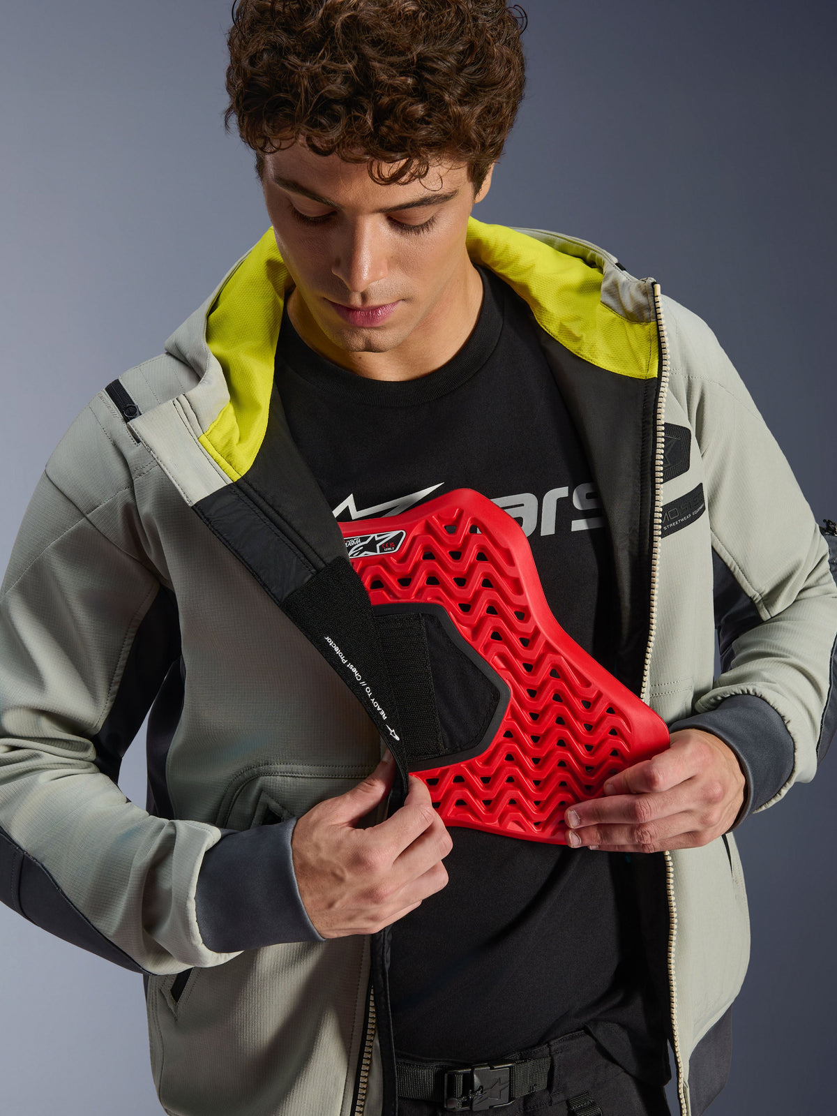 Alpinestars Moblast Waterproof Jacket, kolor Iron Gray i Dark Sage, model prezentujący integrację ochraniacza klatki piersiowej z czerwoną wkładką, jaskrawa limonkowa podszewka, nowoczesna miejska odzież motocyklowa